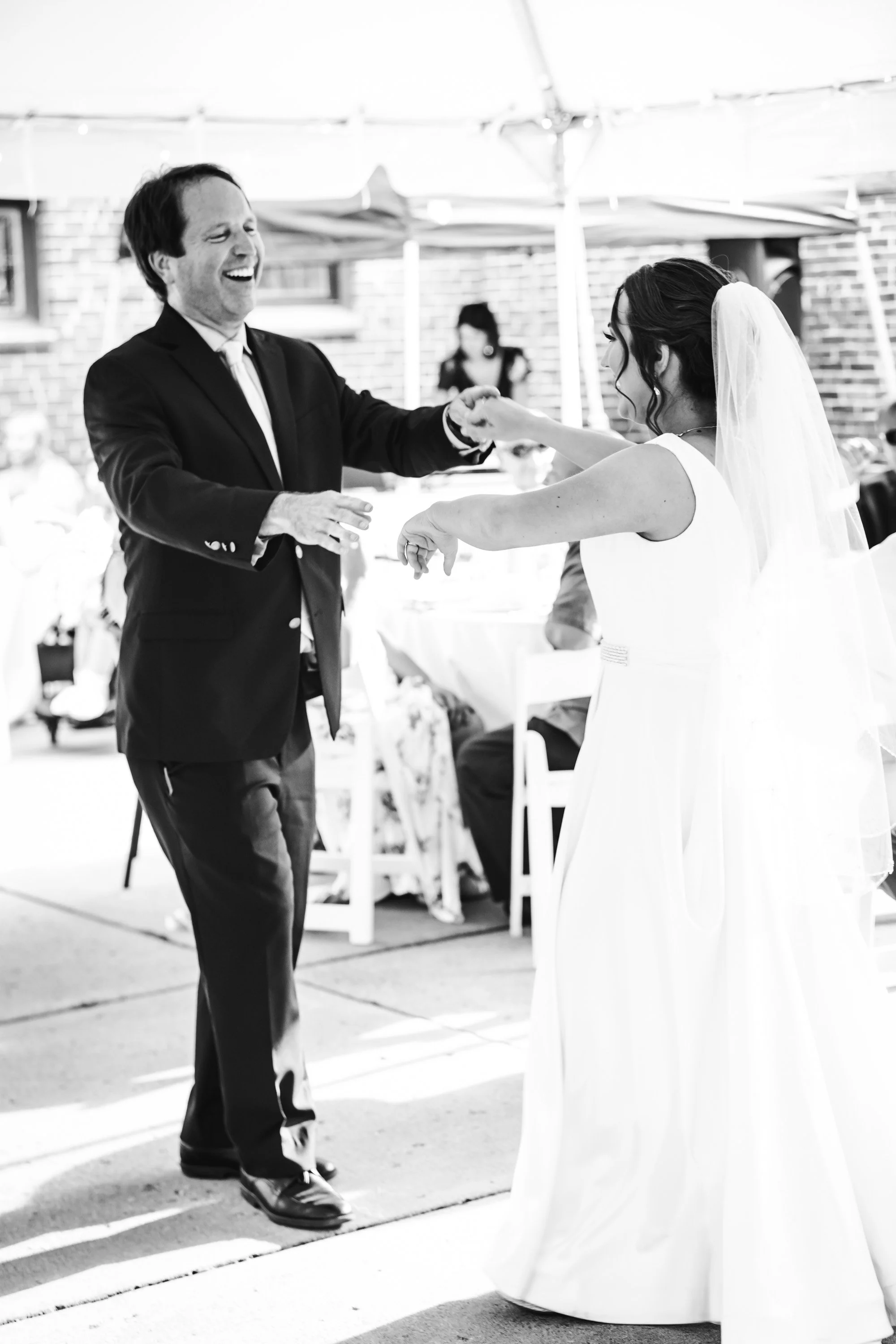 A black and white photo of a man and woman dancing at a wedding reception, with the man in a suit and the woman in a wedding dress and veil.
