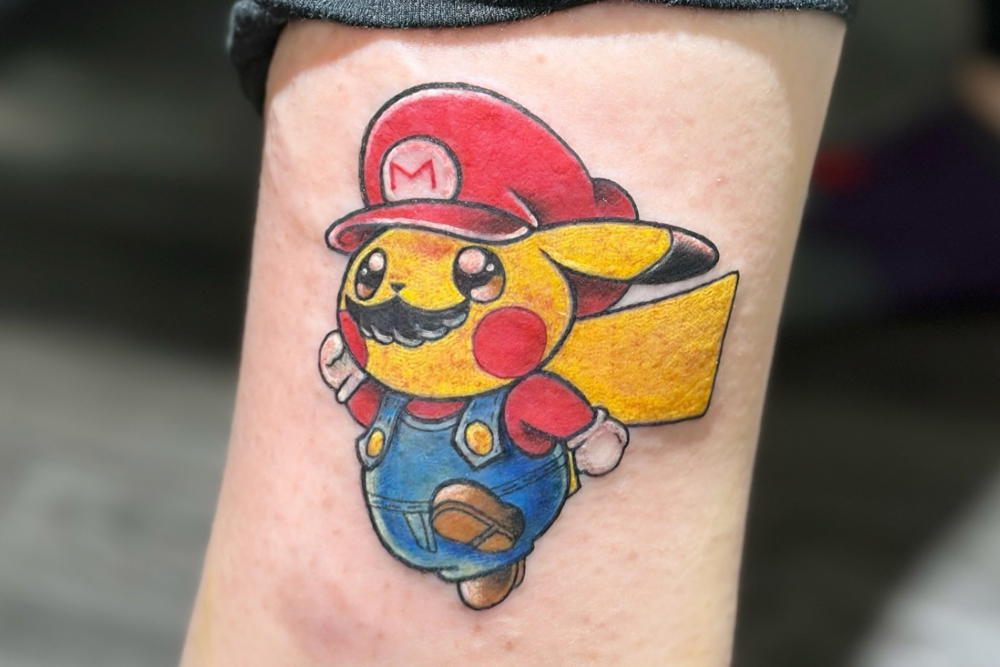 Tattoo of Pikachu dressed as Mario with a red cap, mustache, and yellow tail, on a person's leg.