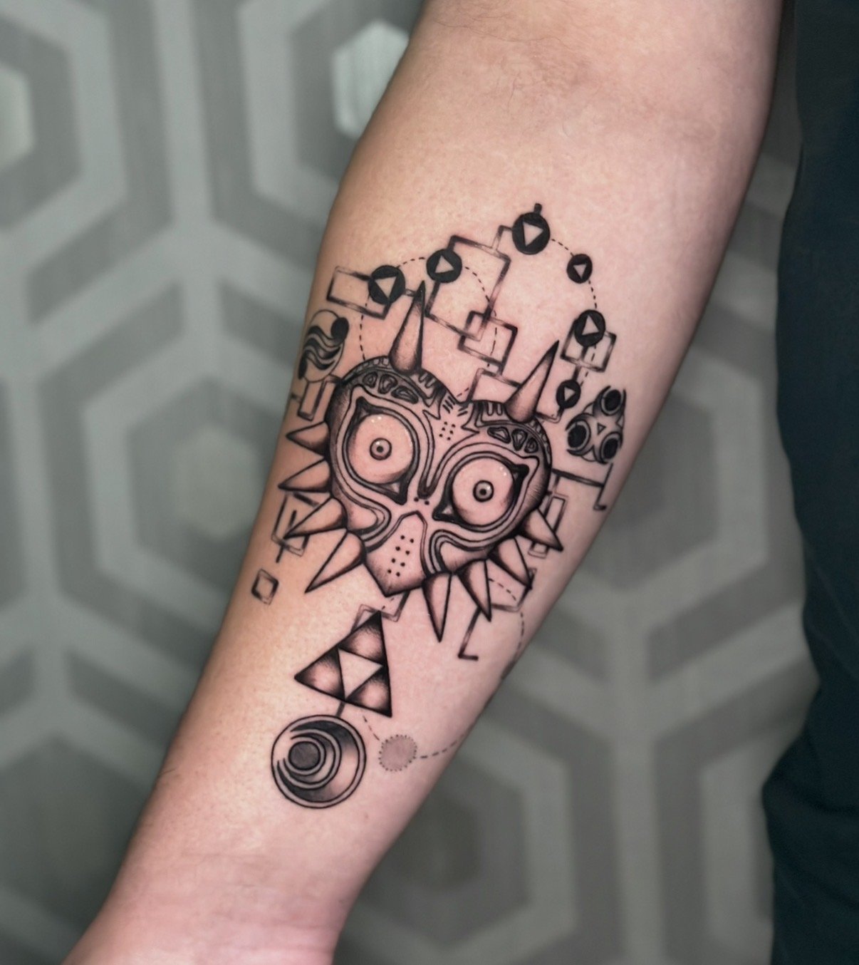 A tattoo of Majora's Mask from The Legend of Zelda video game, with various geometric and abstract design elements surrounding it.