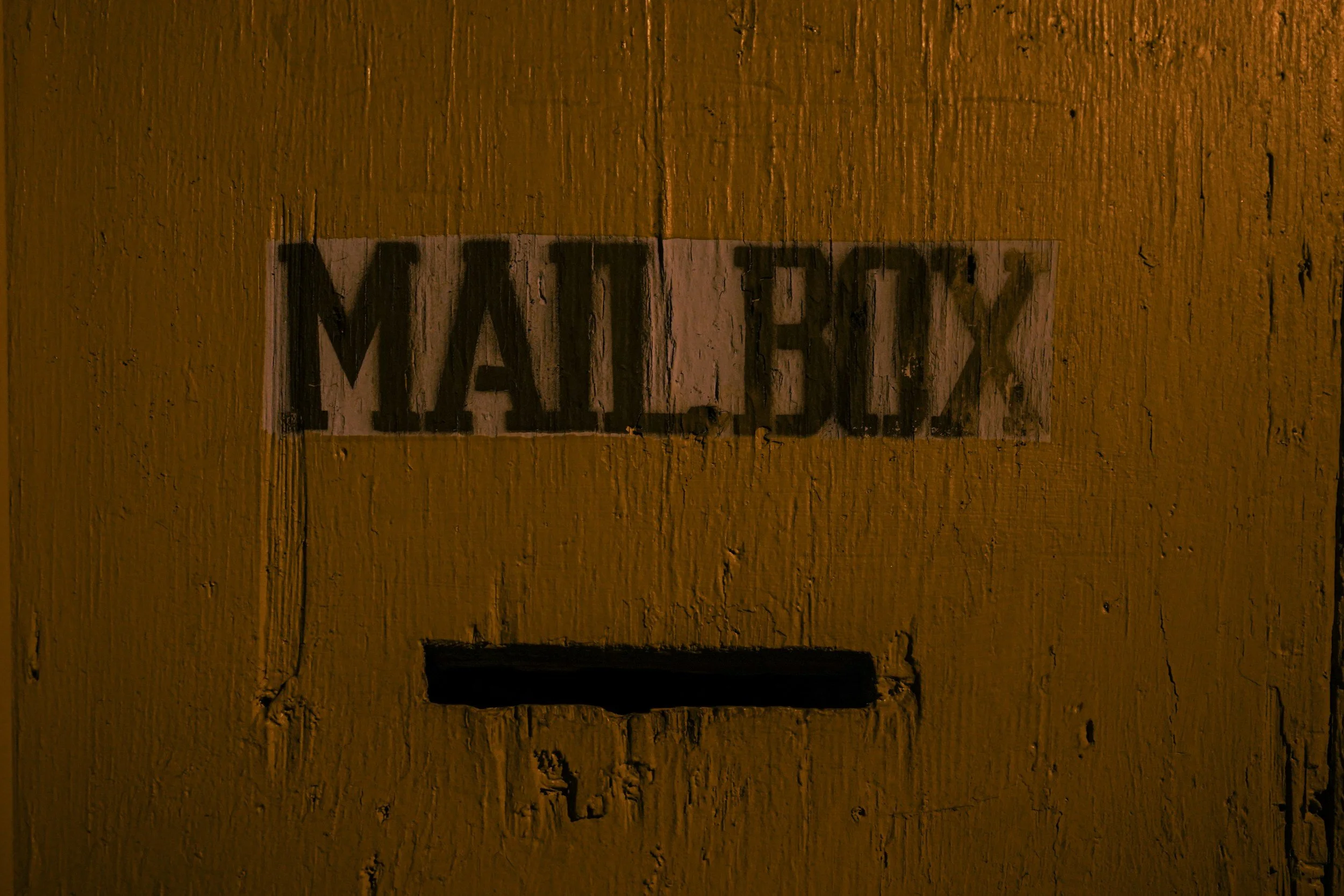 Hand-painted sign on a yellow wooden wall with the word 'MEHV' in black letters.