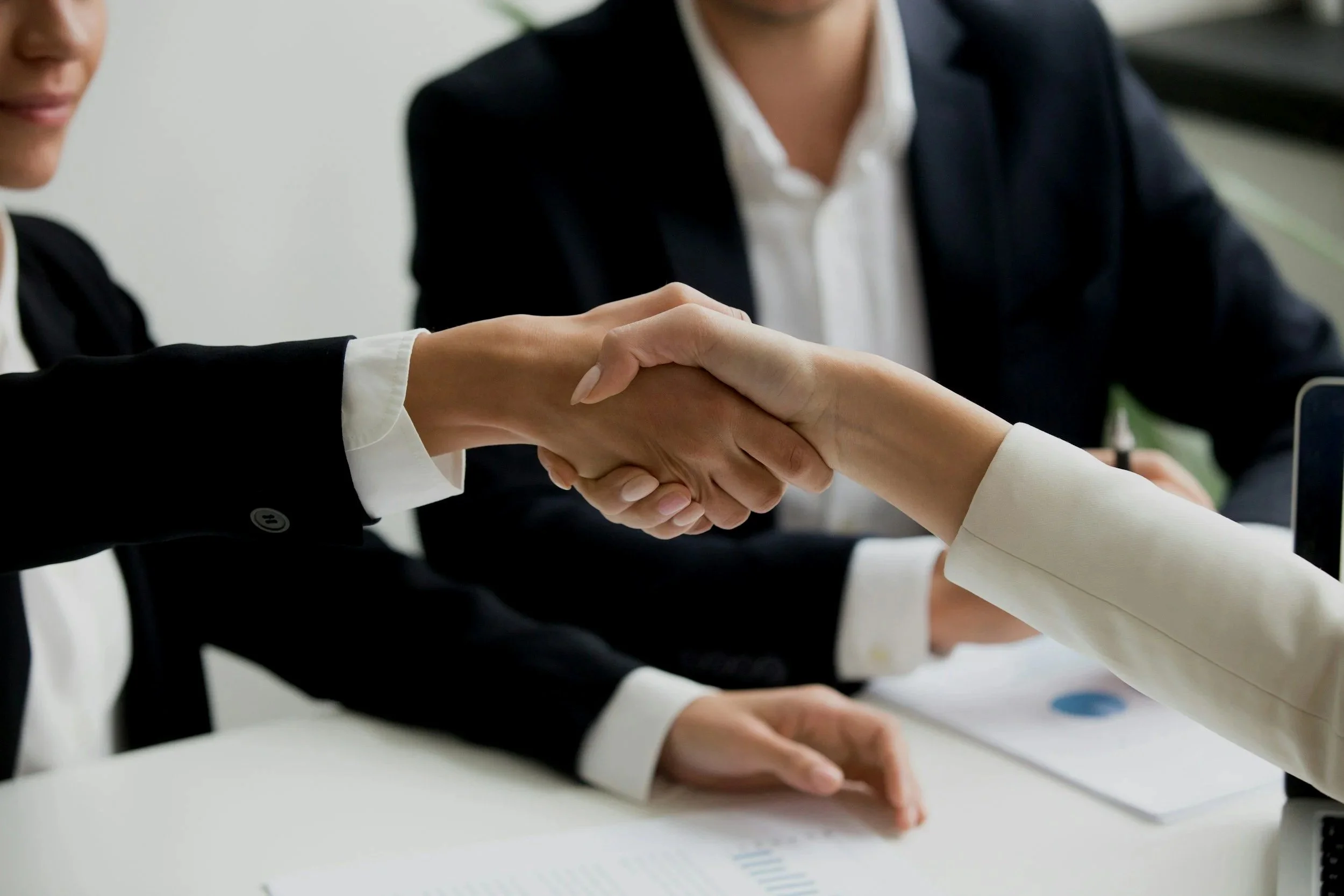 Two women in business suits shaking hands during a meeting.