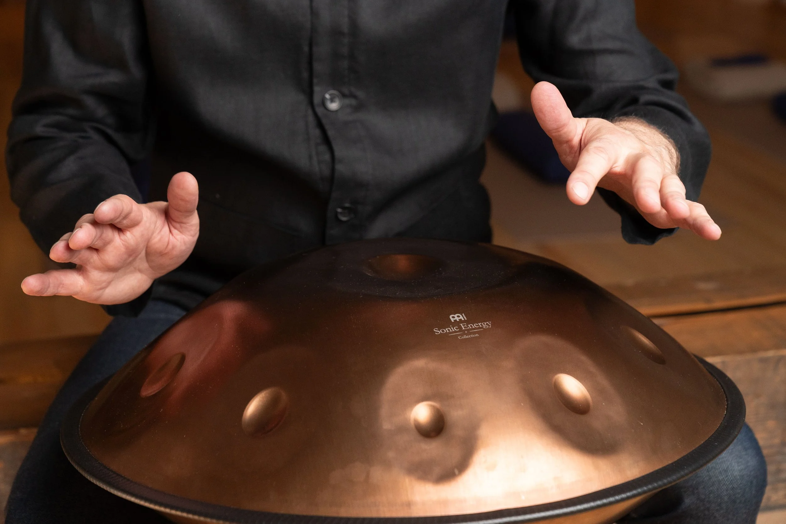 Person playing a handpan instrument, sitting at a wooden surface.