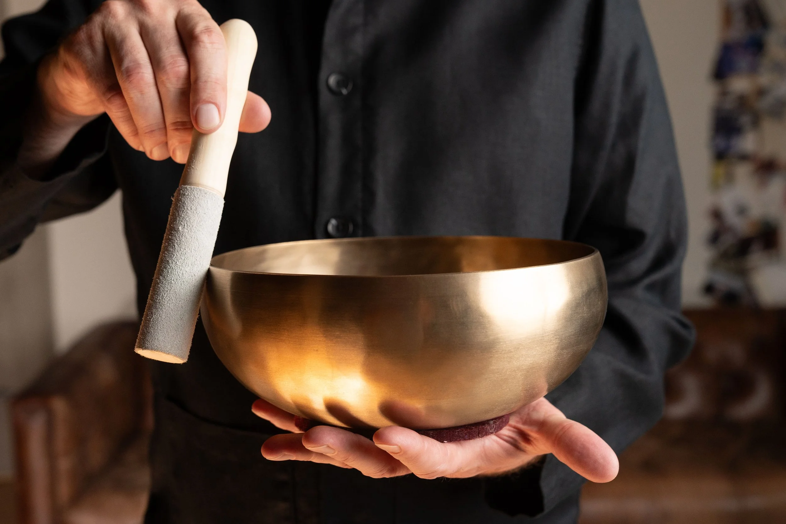 Person holding a brass singing bowl and a mallet, preparing to play it.