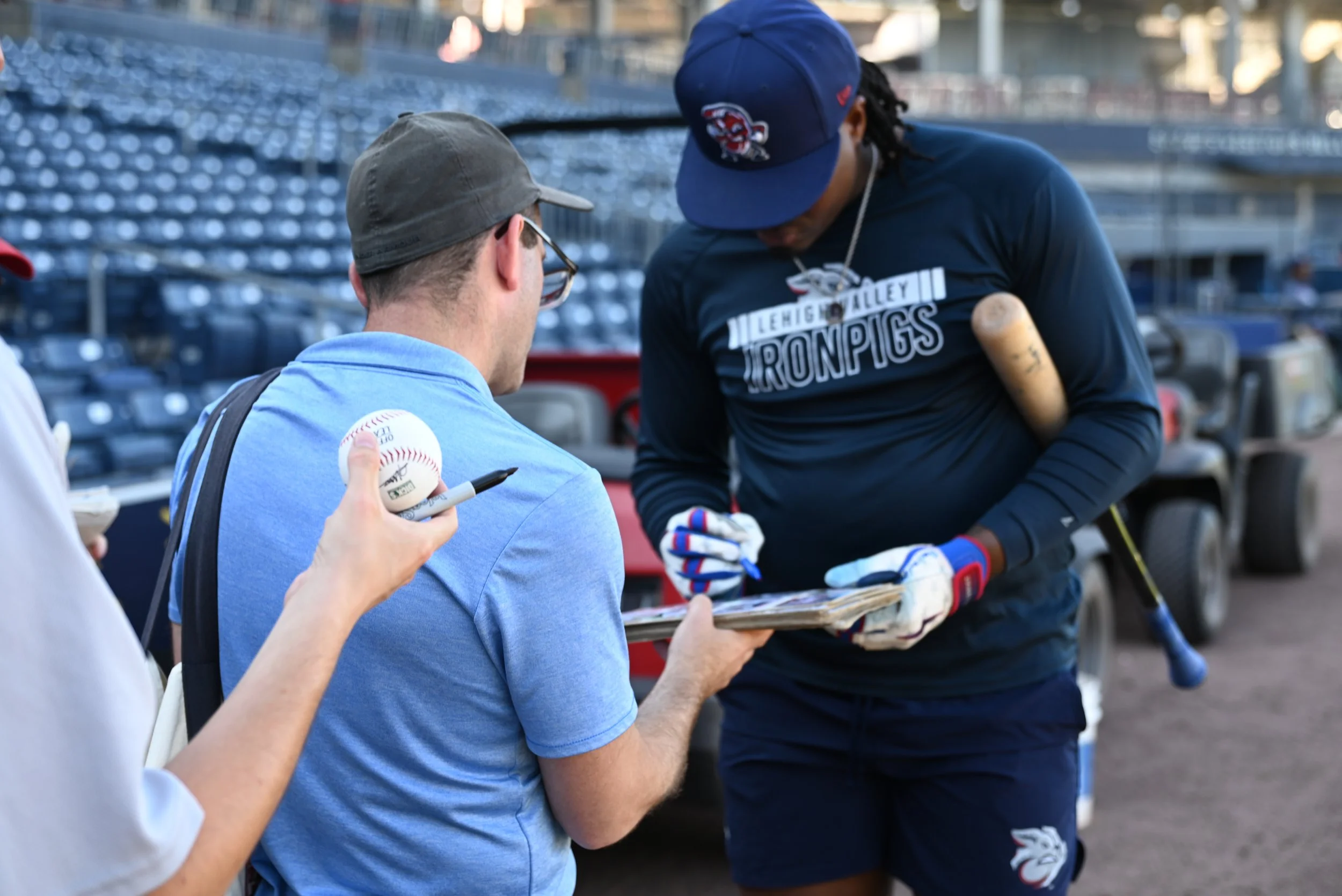 A baseball player wearing a navy blue cap and black shirt with the text "Lehigh Valley IronPigs" signed by fans.