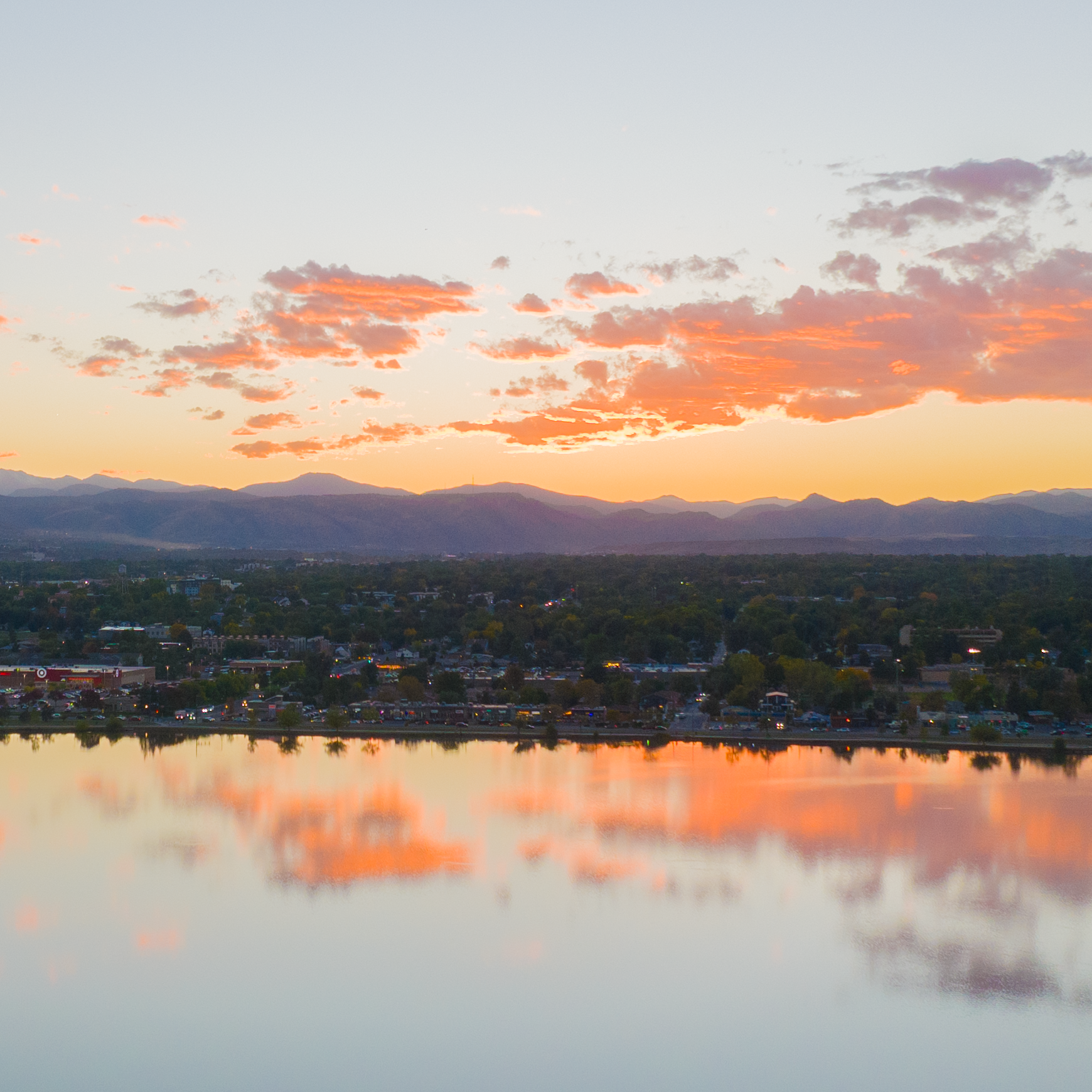 Sunset over mountains reflected in a calm lake with a cityscape in the foreground