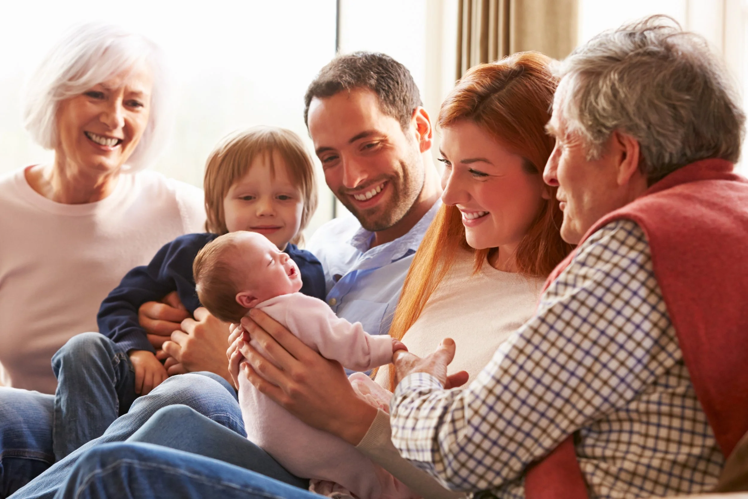 Family surrounding a mother holding her baby, showing support and connection as parents learn baby massage at home to feel more confident and calm.