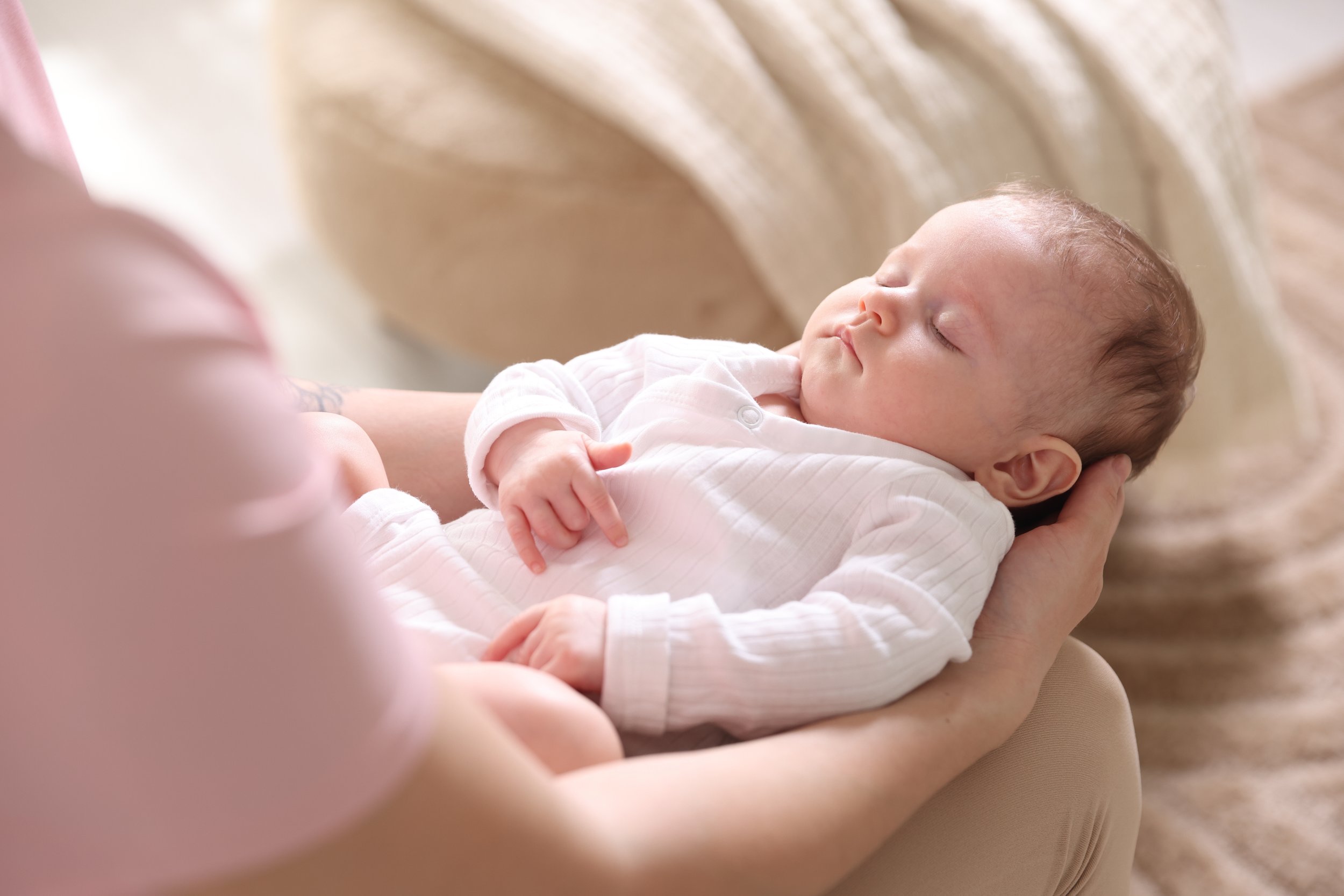 Mother holding a sleeping baby in a calm bedtime setting, showing how baby massage supports relaxation and sleep at Best Beginnings