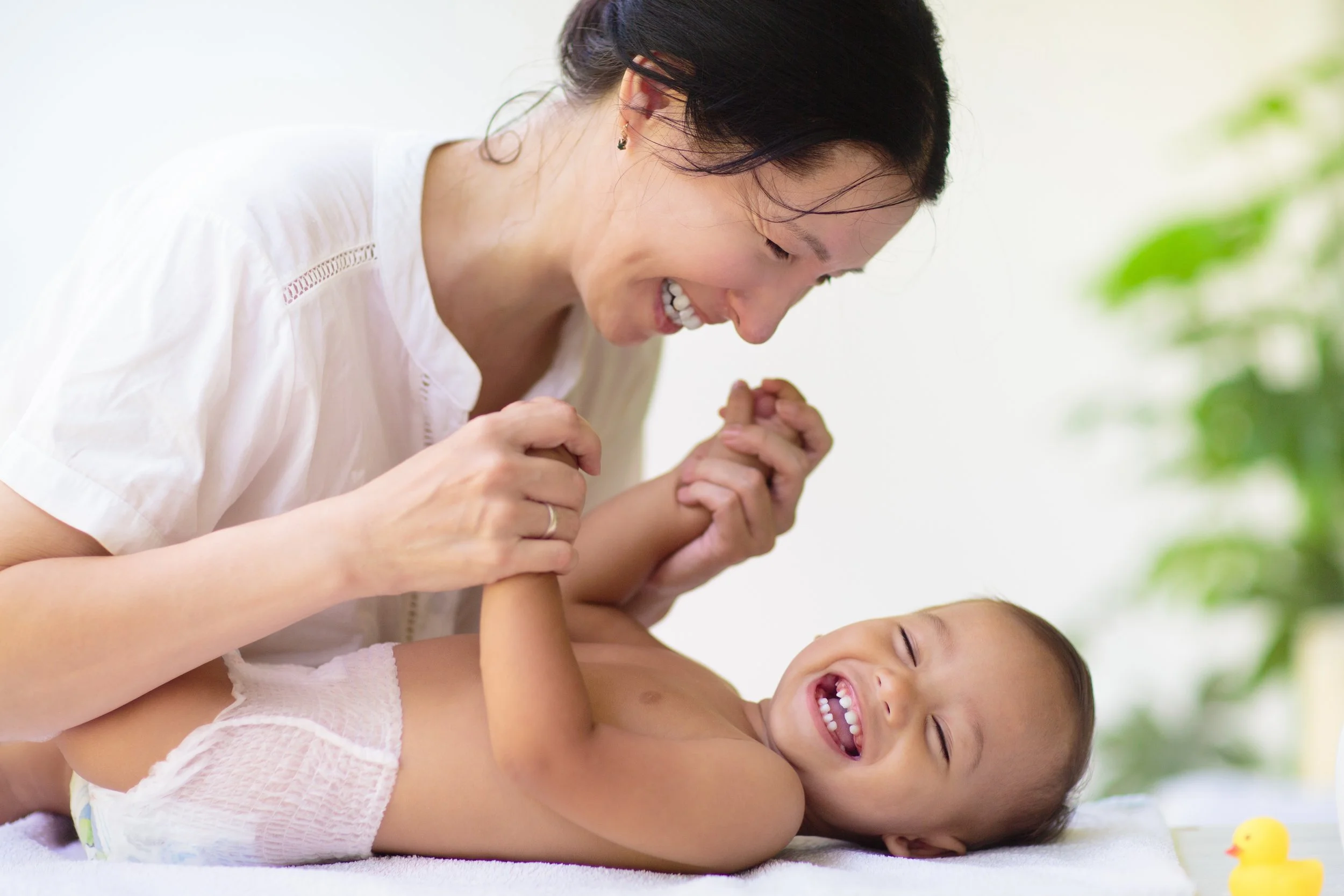 Mother smiling while massaging Baby, showing a calm, happy moment of connection through baby massage in everyday life