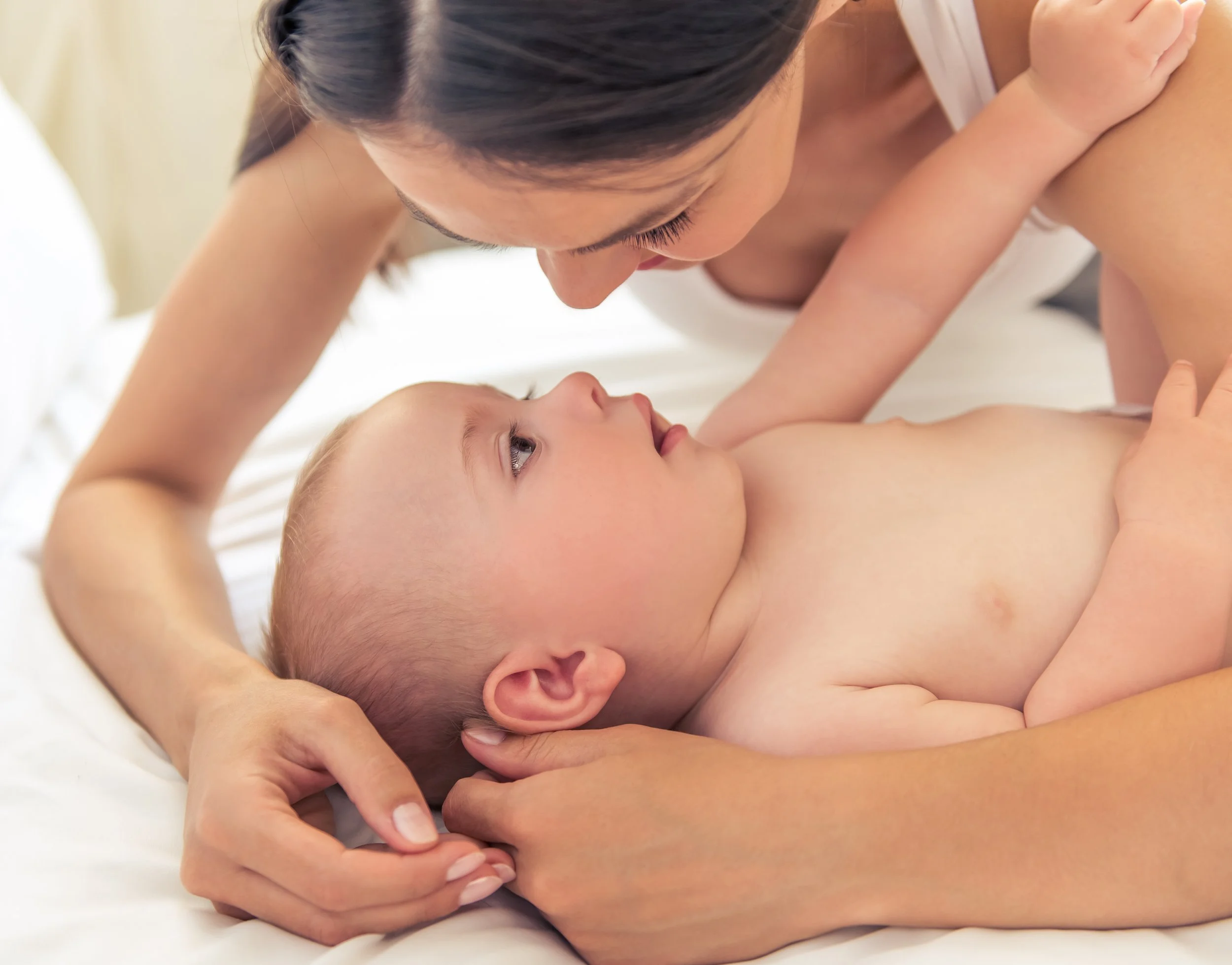 Mother leaning over Baby during baby massage, showing calm connection and bonding through gentle touch