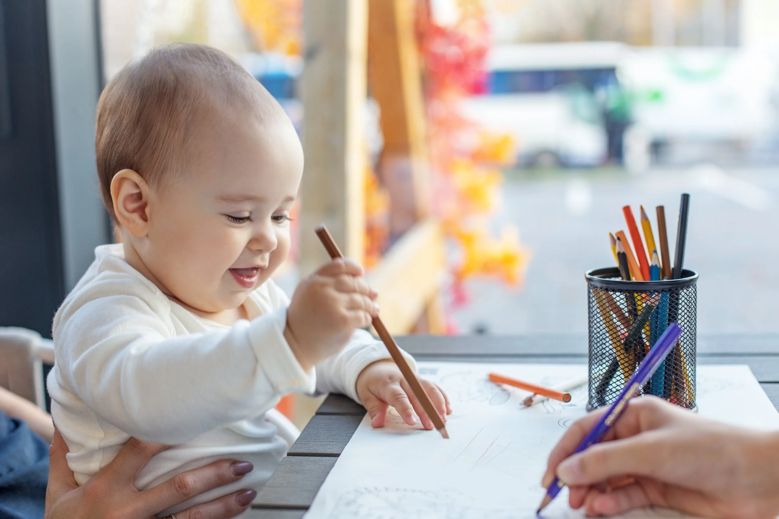 Baby learning to hold a colored pencil, showing early fine motor development and hand coordination