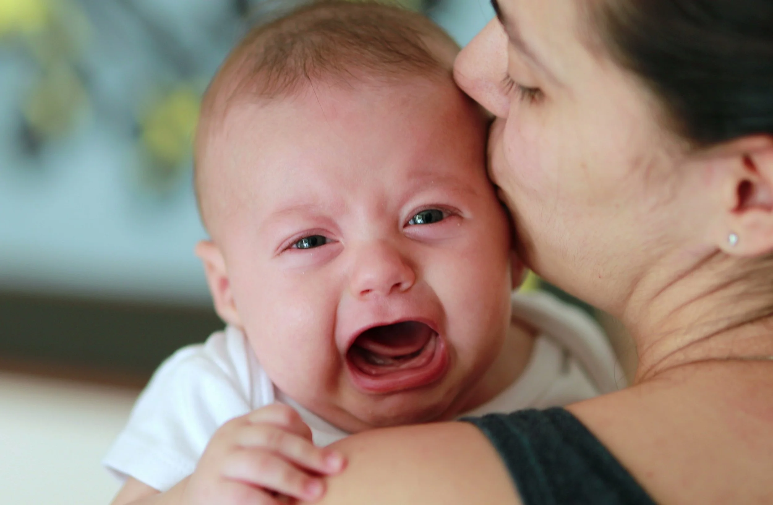 Crying baby being held by mom, showing discomfort from gas and the need for soothing support through gentle touch