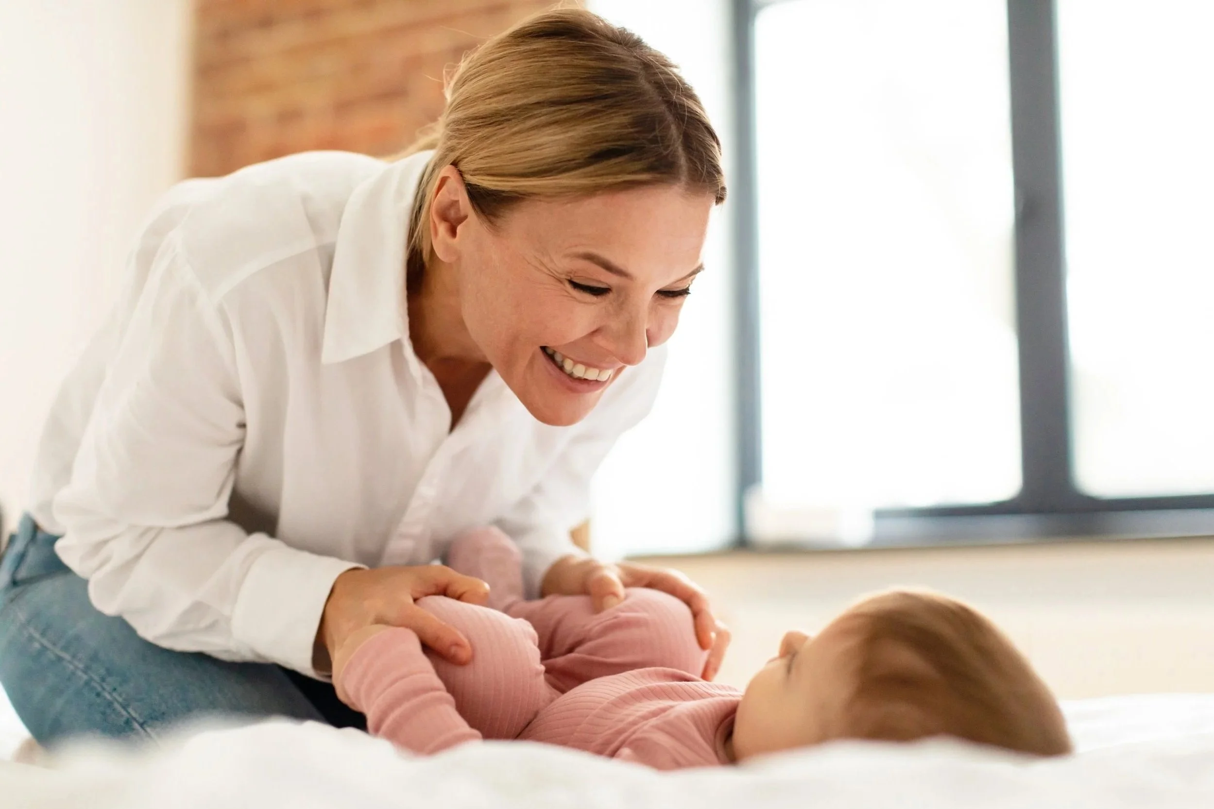 Mother leaning over and smiling at Baby during baby massage, showing a calm and connected moment at home