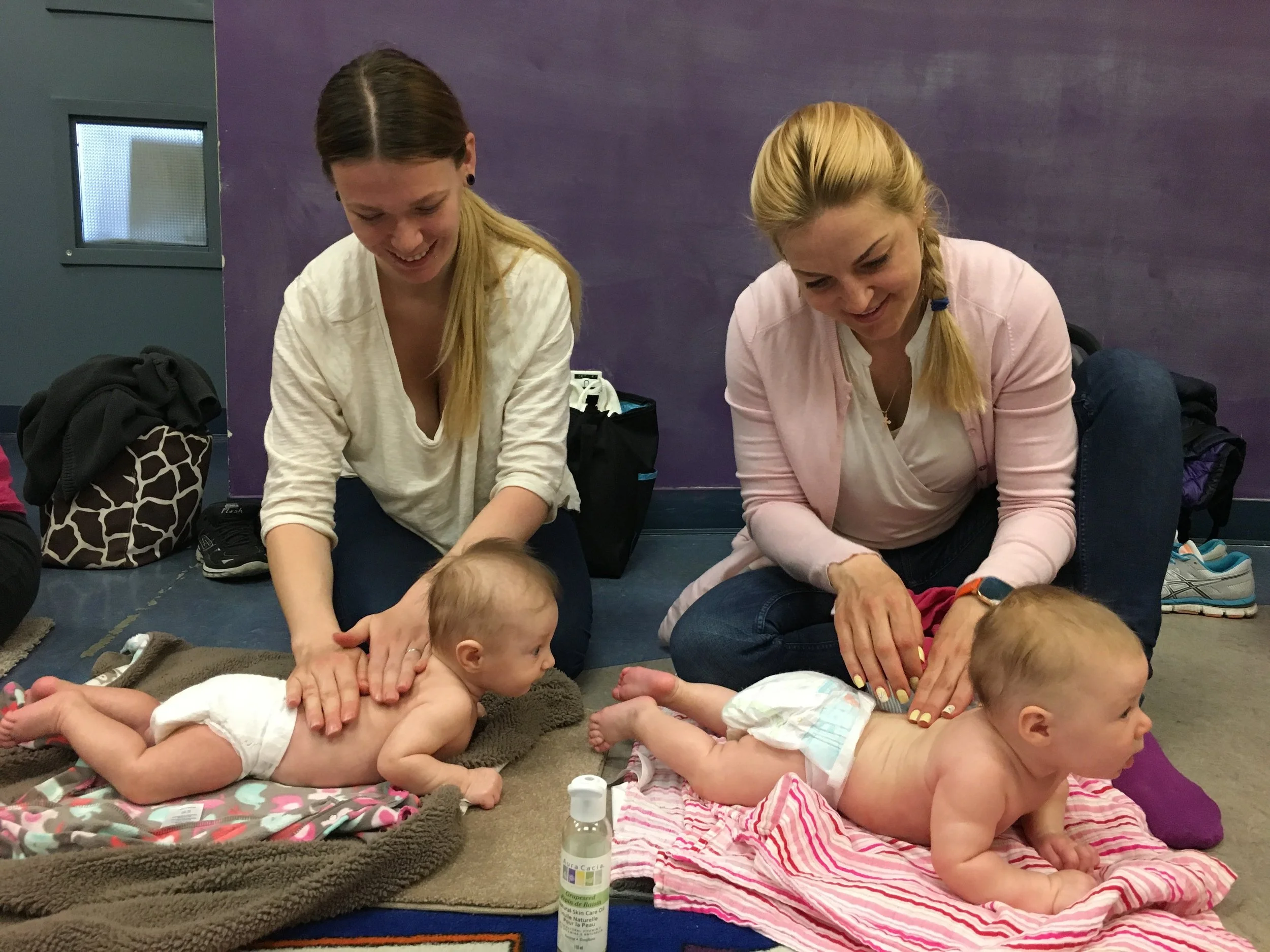 Two moms practicing baby massage in a class setting, learning how to set up a calm and comfortable massage space with their babies