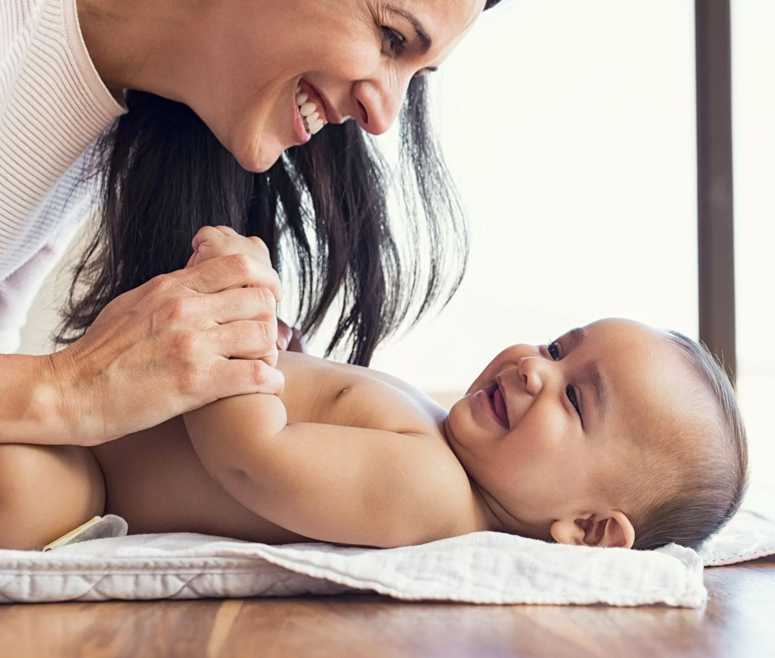 Mother smiling at Baby lying on their back during infant massage, showing how gentle touch strengthens bonding, reduces stress, and helps parents feel more confident and connected