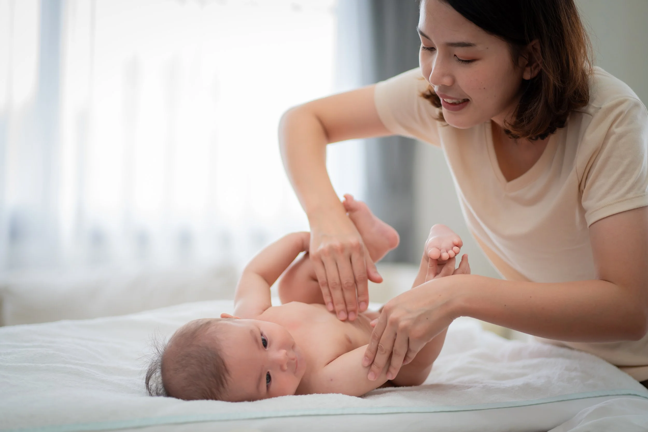 Mother gently massaging her baby at home, supporting digestion, calming, and better sleep through baby massage
