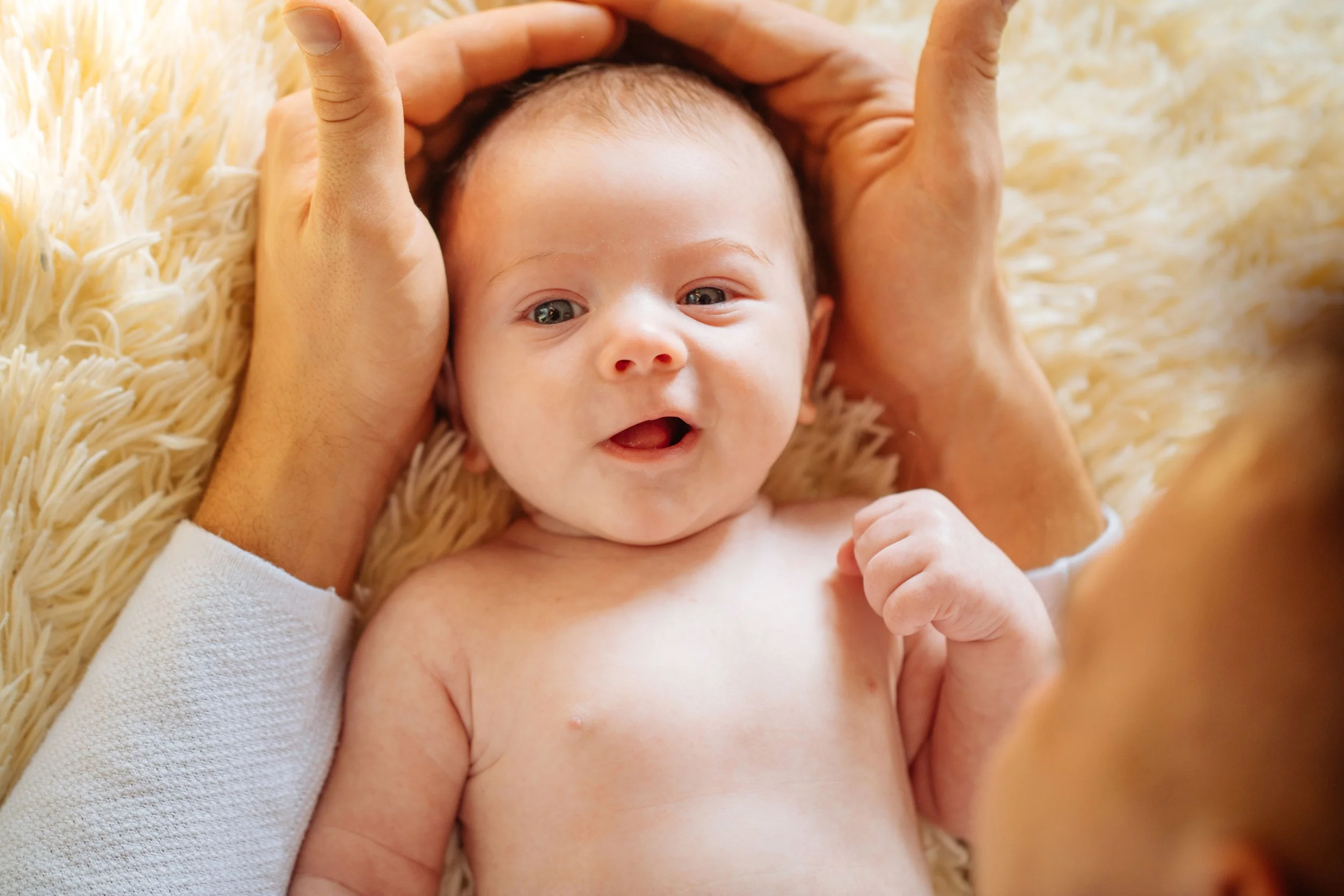 Baby lying on their back with parents’ hands gently cupped around their face, showing love, connection, and a meaningful baby shower gift