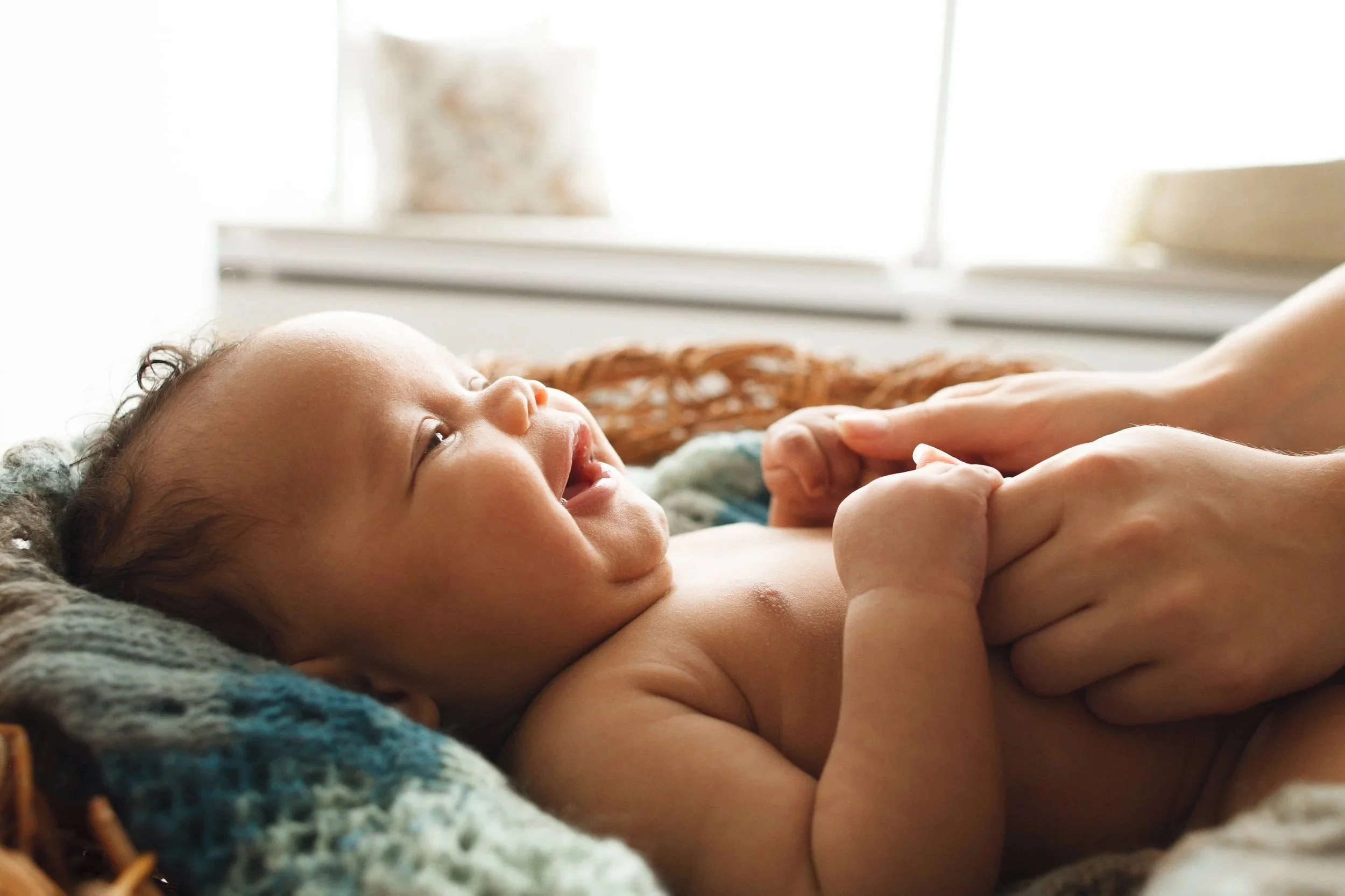 Baby lying on their back smiling up at mom during baby massage, showing connection, comfort, and calm interaction
