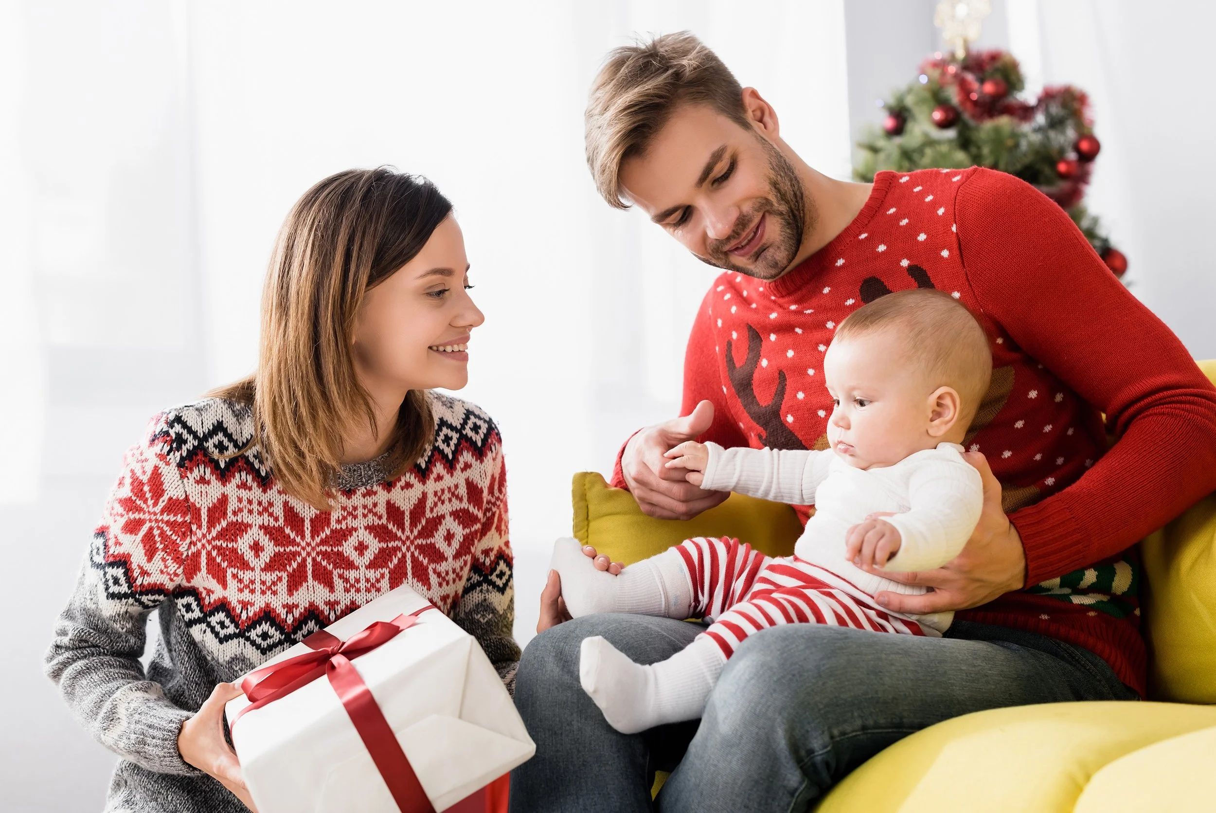 Parents holding their baby and a Christmas present, showing a meaningful and thoughtful holiday gift for a new family
