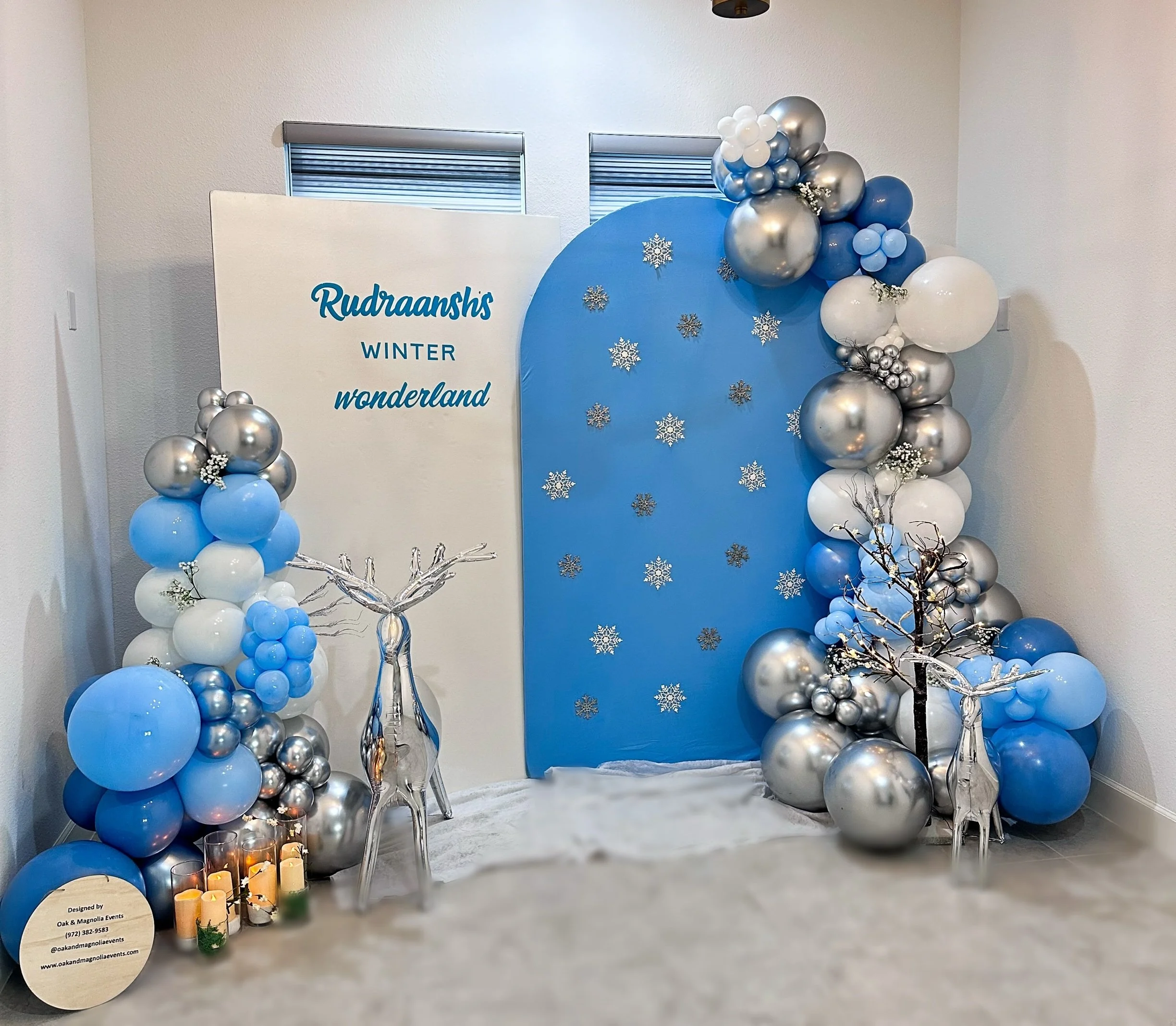 Winter Wonderland themed event backdrop with blue and silver balloons, snowflake decorations, a white sign with blue text, LED candles, and silver reindeer figures.