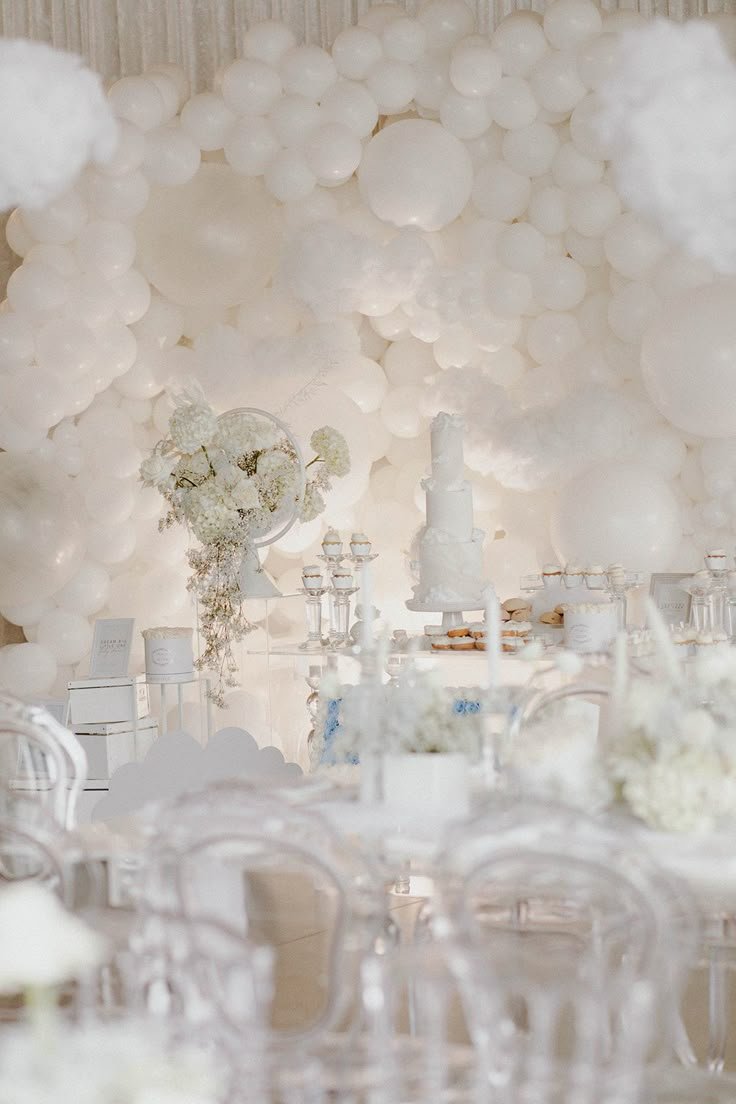 White balloons and flowers creating a background for a decorated table at a celebration event.