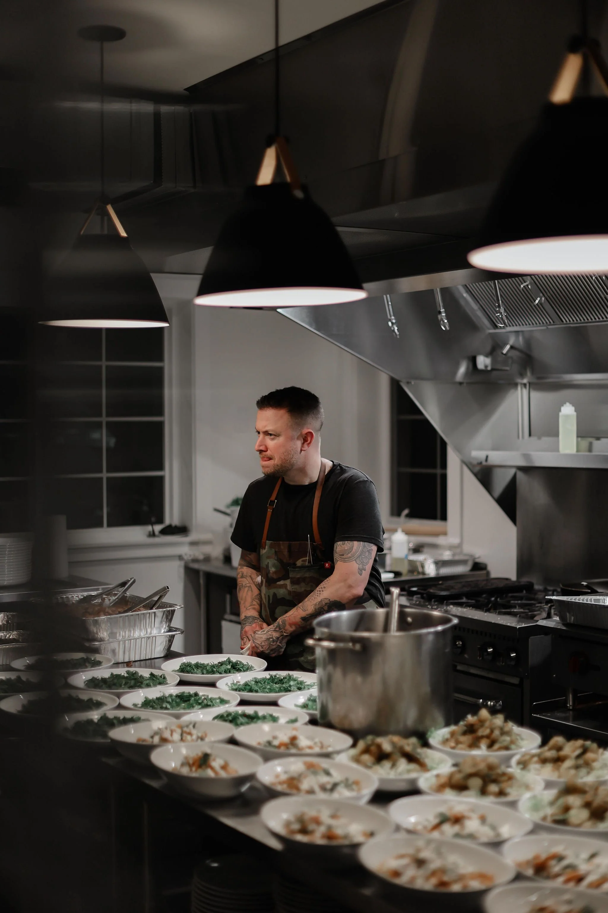 A man with tattoos preparing multiple plates of food in a professional kitchen.