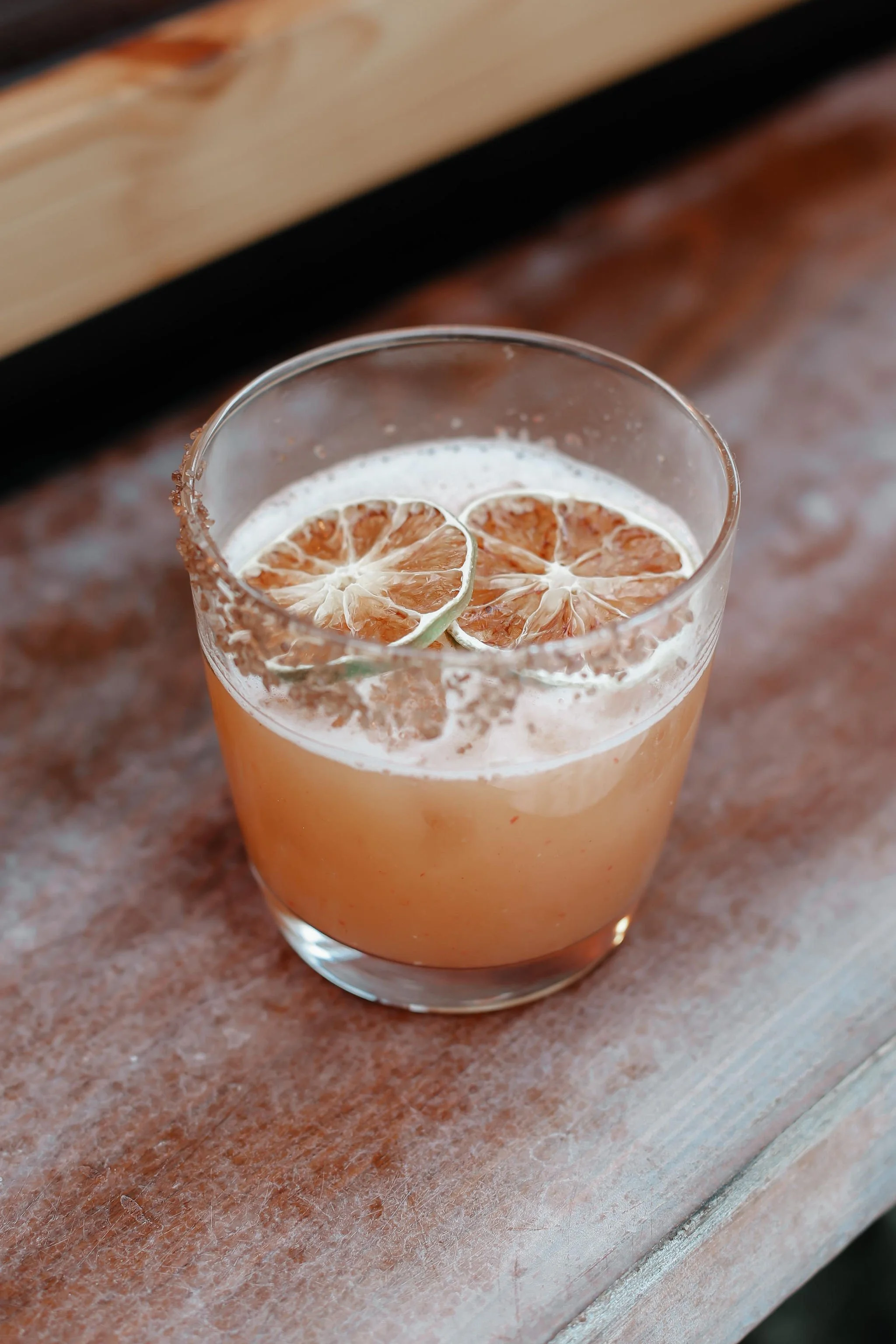 A glass of grapefruit cocktail garnished with dried lime slices on a wooden surface.