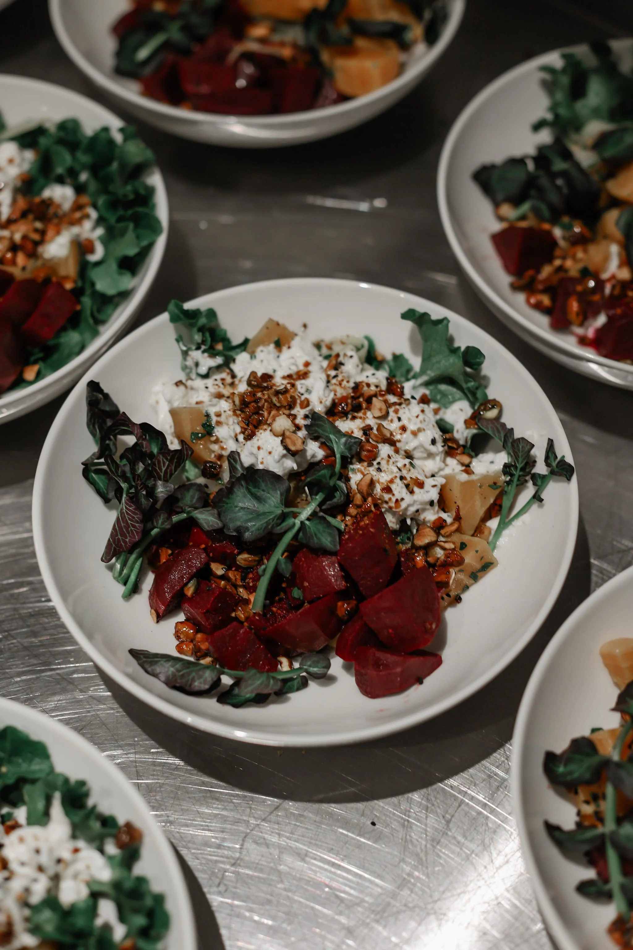 Salad with mixed greens, beets, crumbled cheese, nuts, and chopped vegetables in a white bowl.