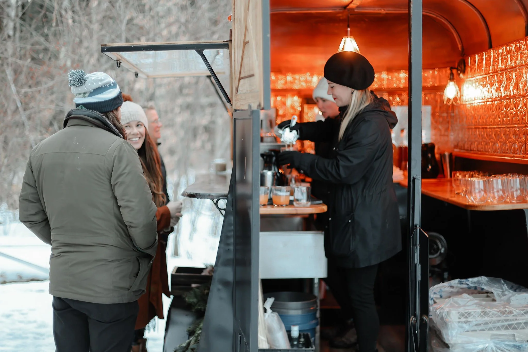 People standing in line at a food truck serving hot beverages, with a snowy outdoor setting and women in winter clothing.