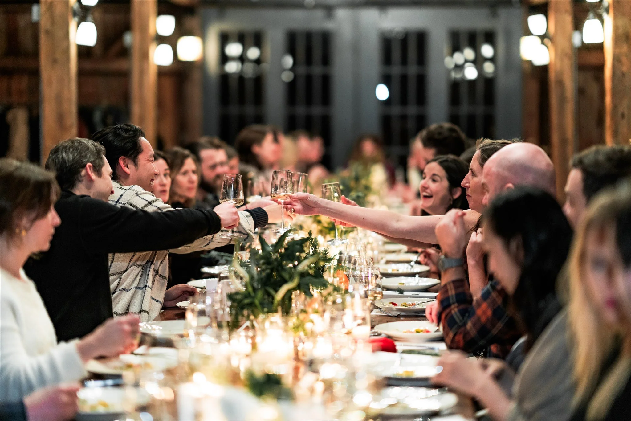 People at a dinner table clinking glasses in a toast at a festive gathering in a rustic setting.