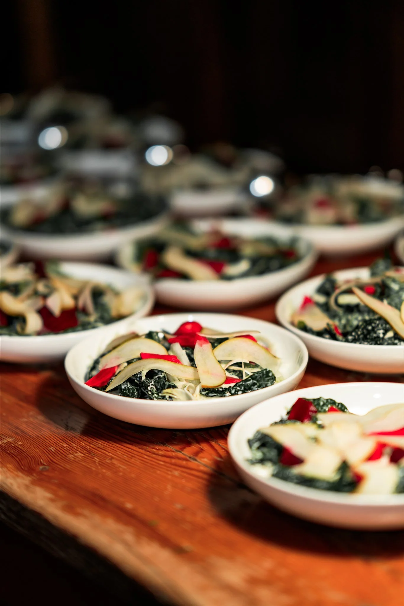 Several white bowls filled with a black and white dish, garnished with red accents, arranged on a wooden table.