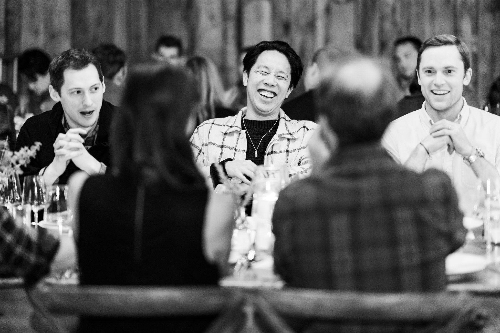 People laughing and talking at a dinner party in a rustic setting.