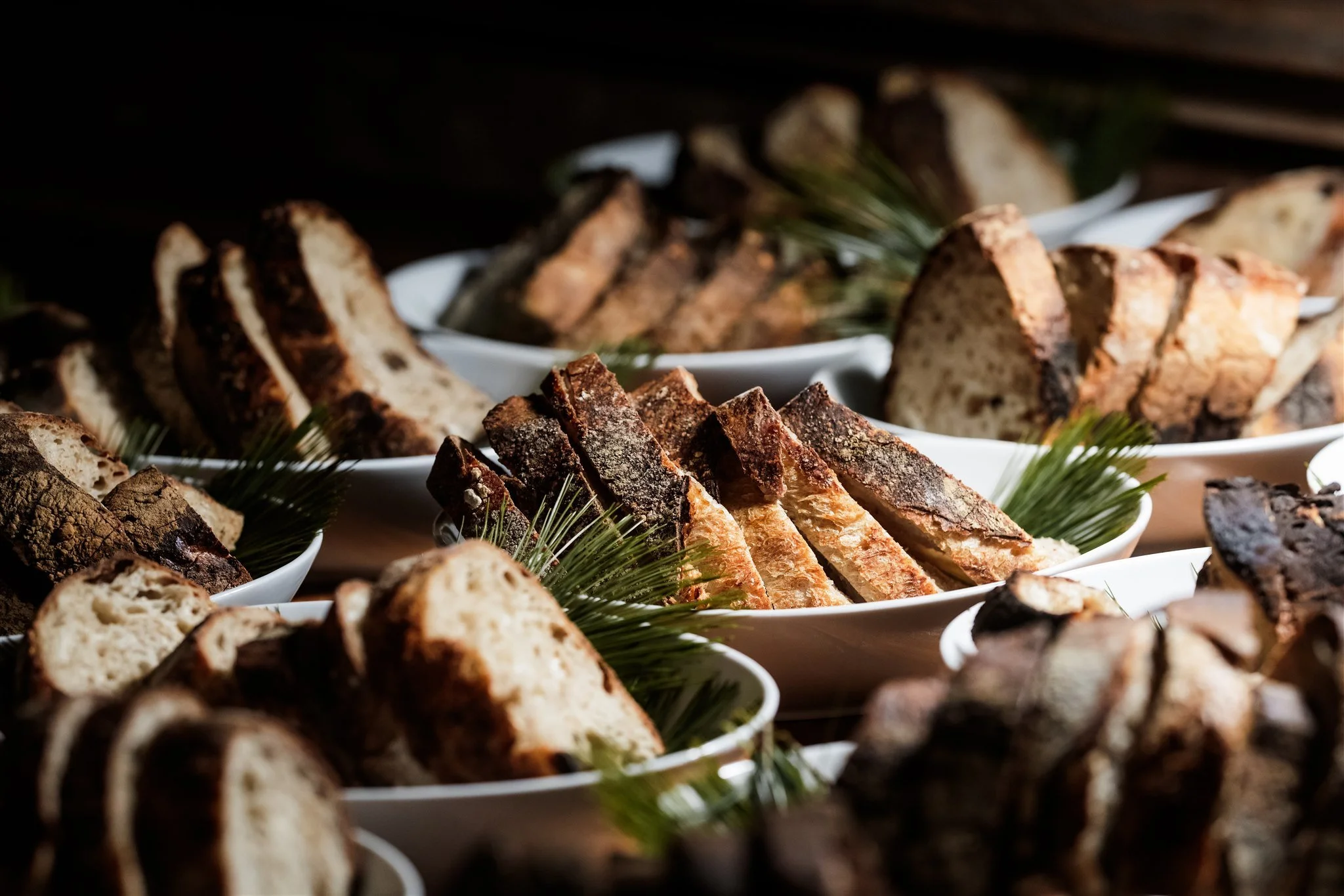 Multiple plates of sliced bread and baked goods with pine branch decorations.