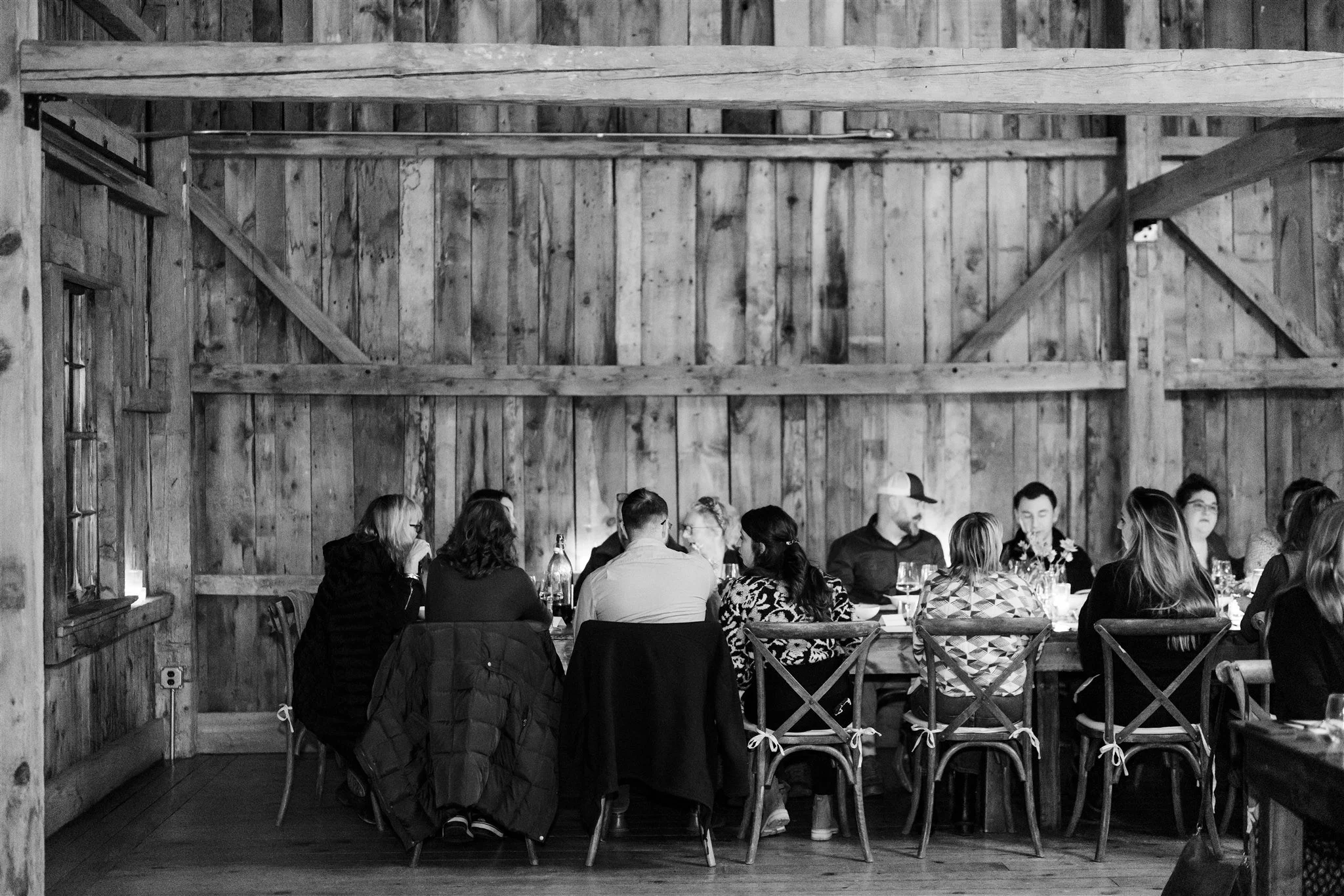 People sitting around a lunch or dinner table in a wooden rustic setting, engaging in conversation, with some beverages and tableware visible.