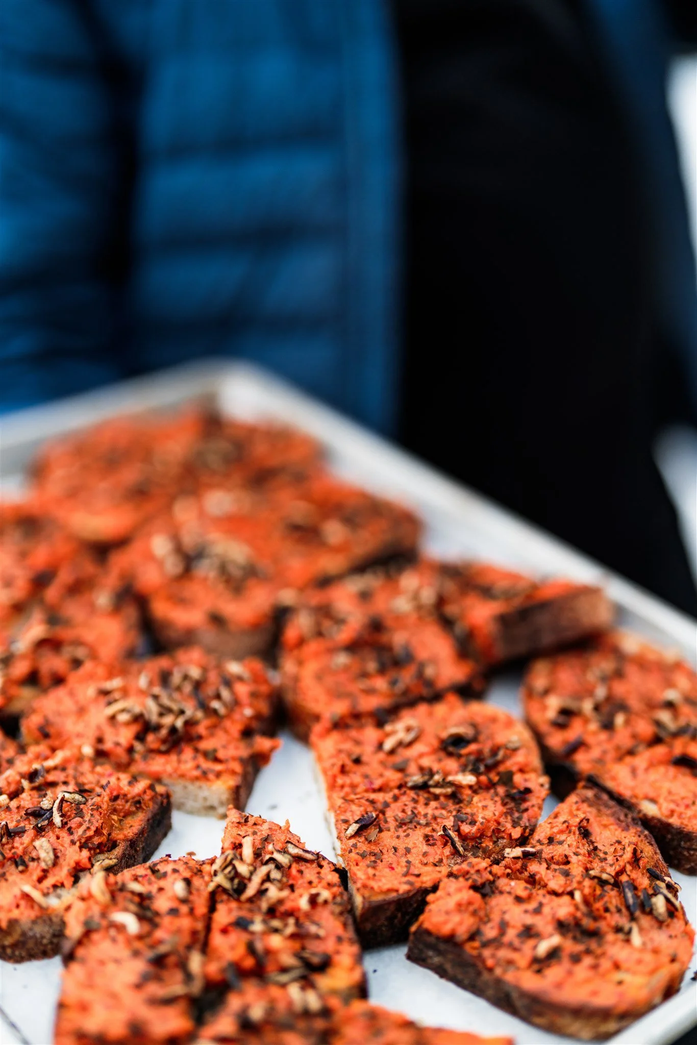 Slices of roasted red pepper seasoned with herbs and topped with black sesame seeds on a white platter.