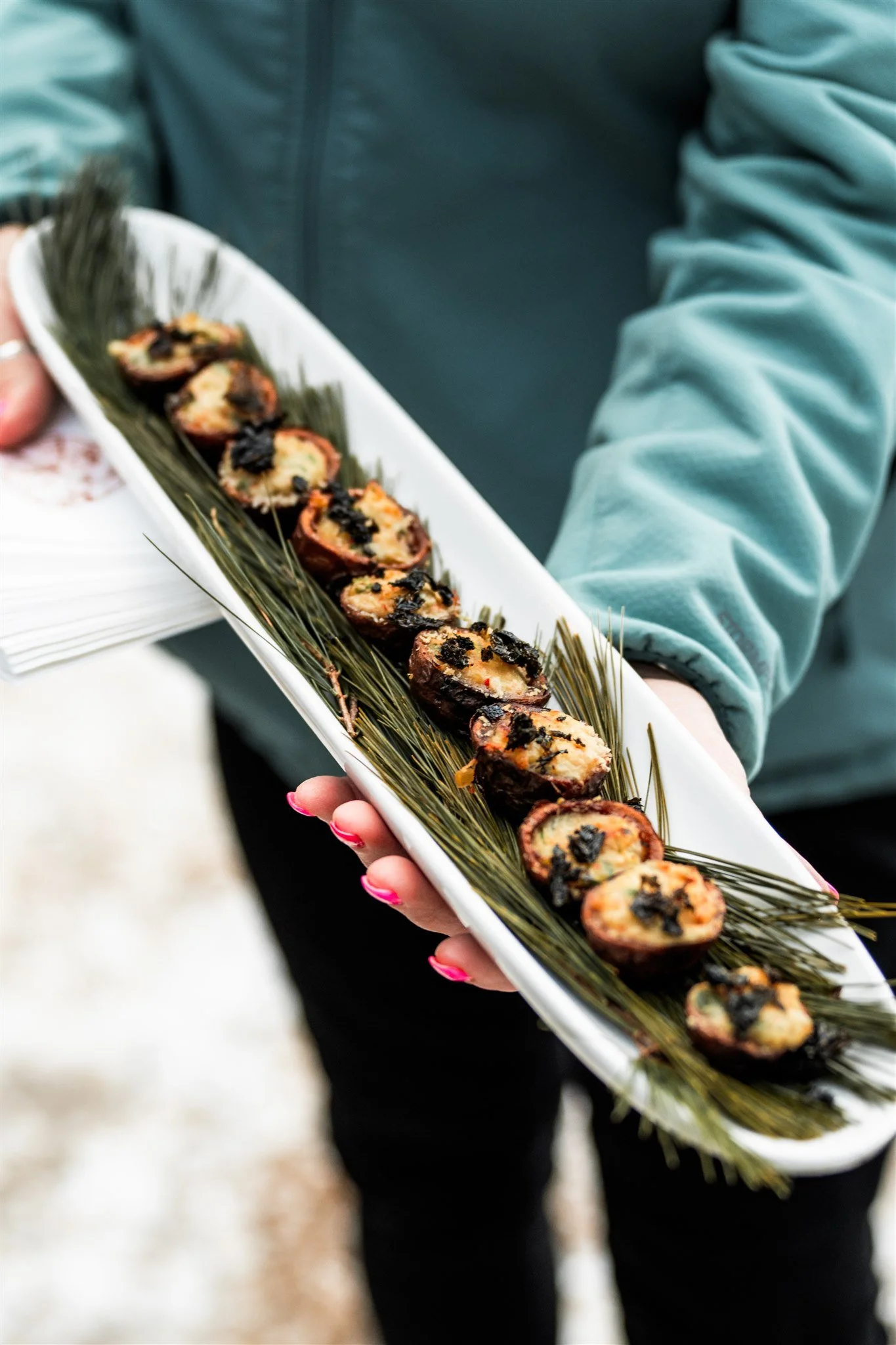Person holding a long white platter with sliced sushi rolls on a bed of green grass-like garnish.