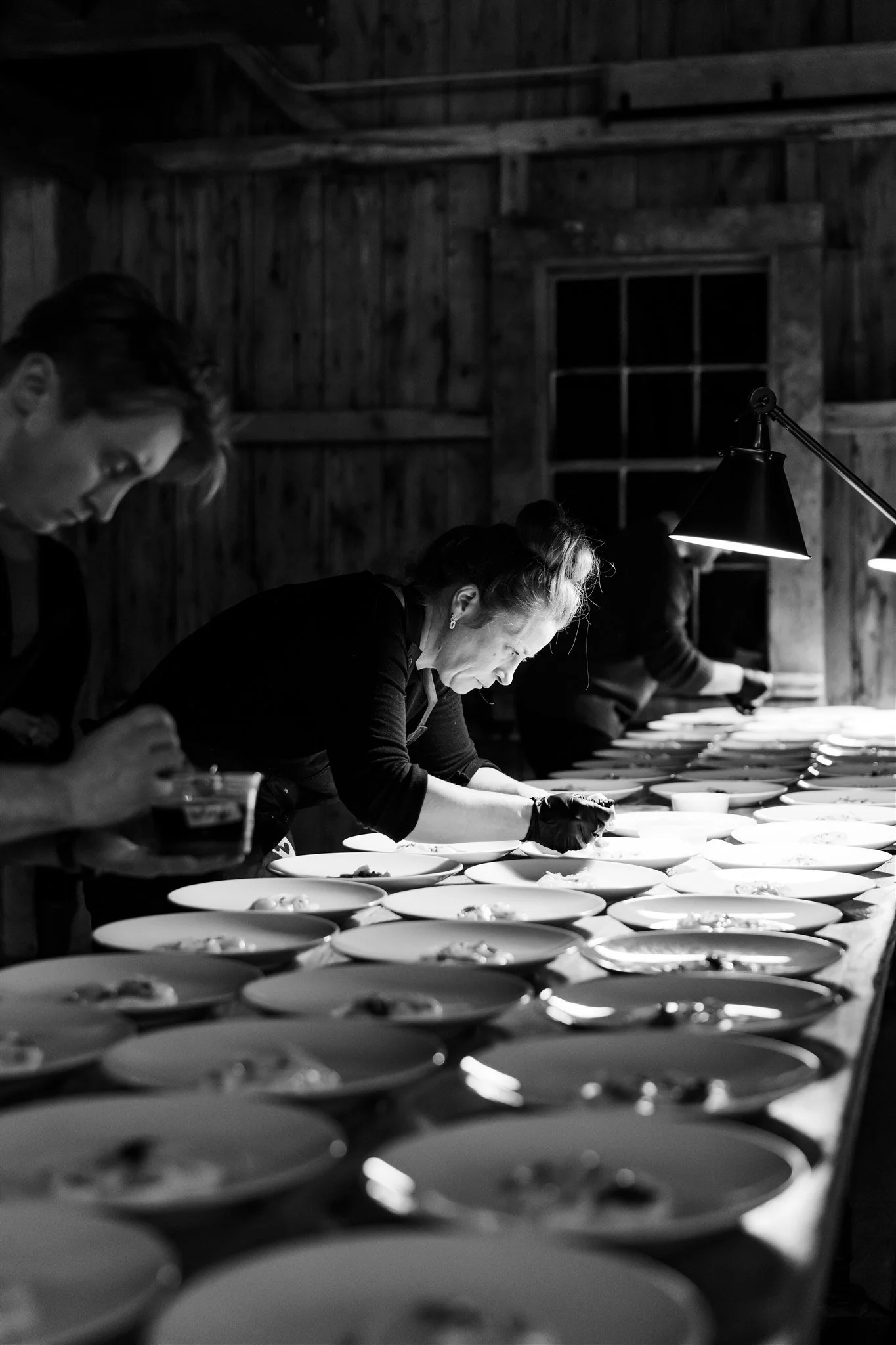Black and white photograph of chefs plating dishes in a rustic wooden kitchen