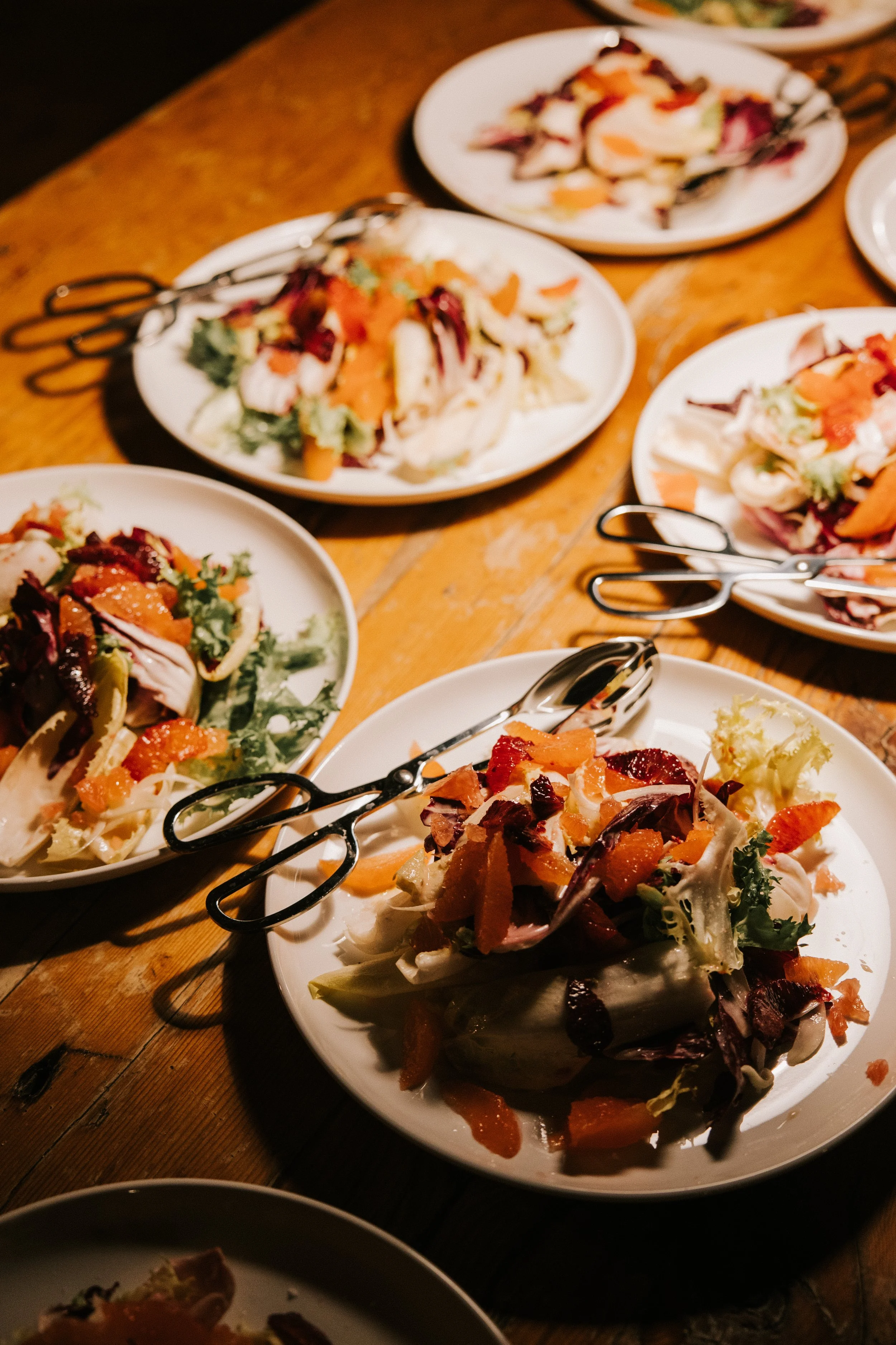 Multiple plates of colorful salads with mixed greens, vegetables, and dressing on a wooden table.