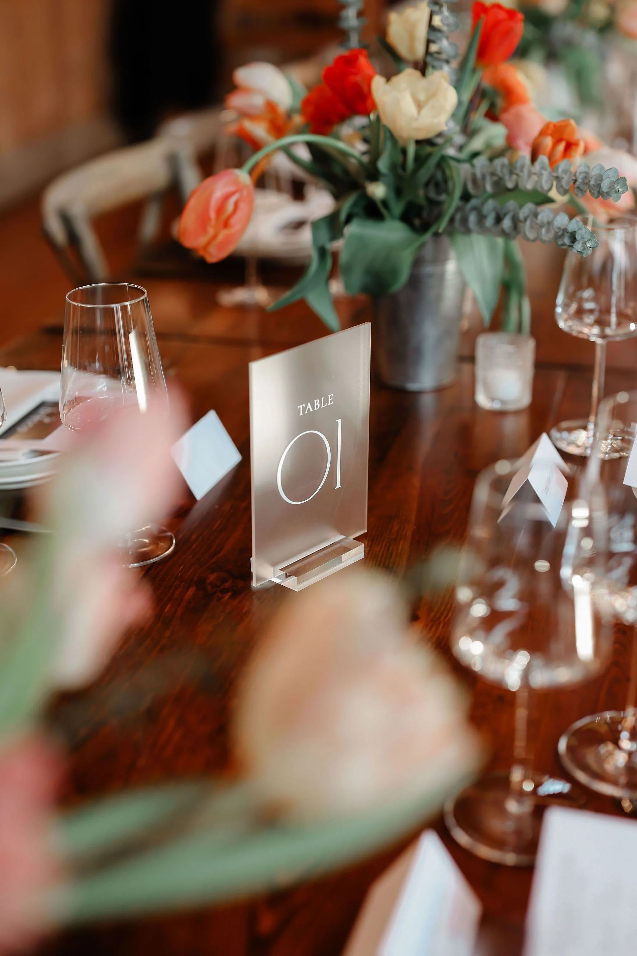 A table setting with a floral centerpiece, wine glasses, and a table number sign indicating 'Table 01' at an elegant event or wedding.