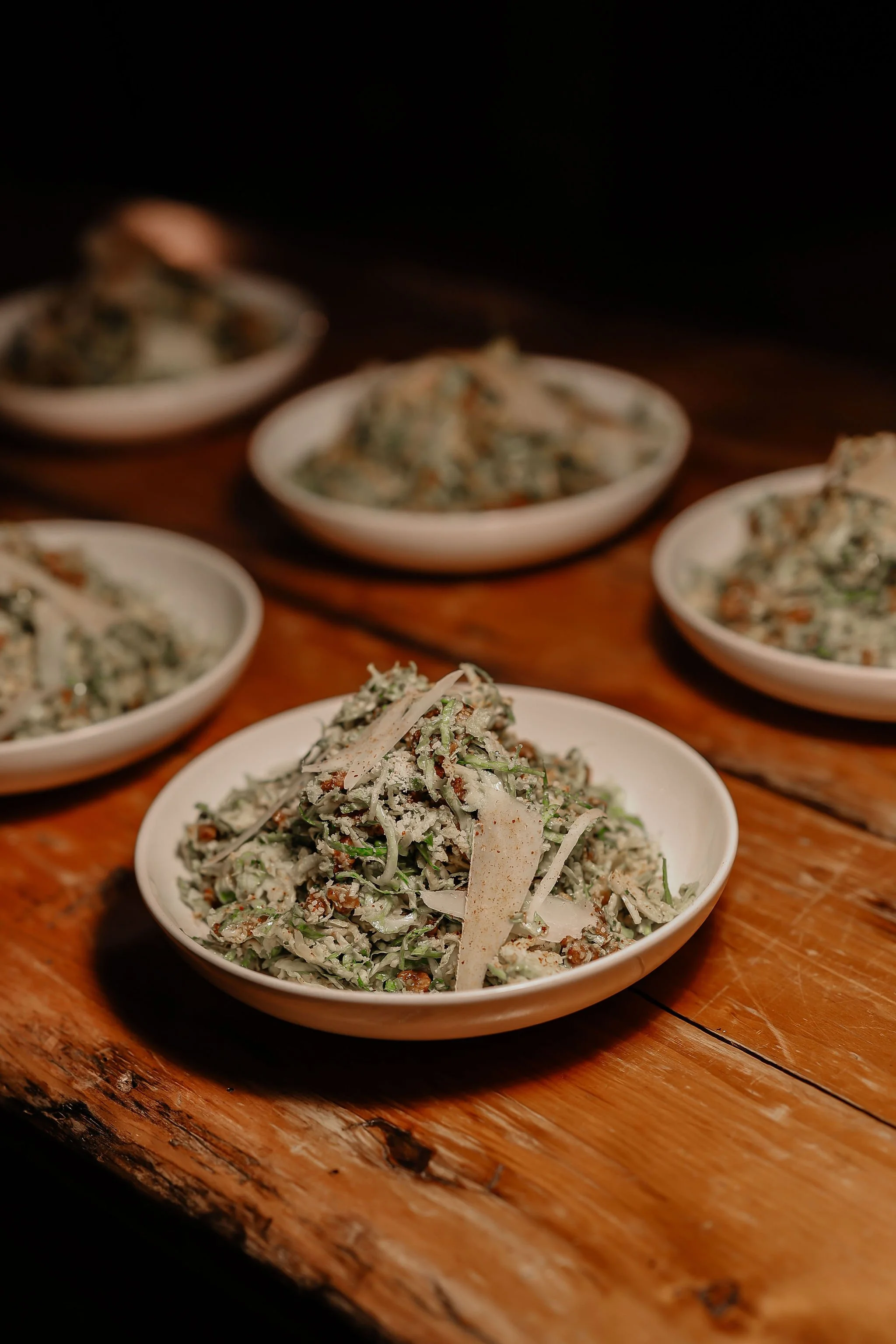 Multiple small white bowls of shredded vegetable salad on a rustic wooden table, with a dark background.