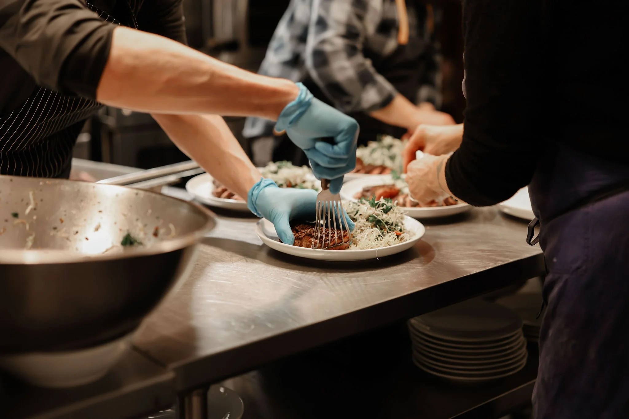 Chefs preparing plates of food in a kitchen, placing grilled meats and salads on plates.