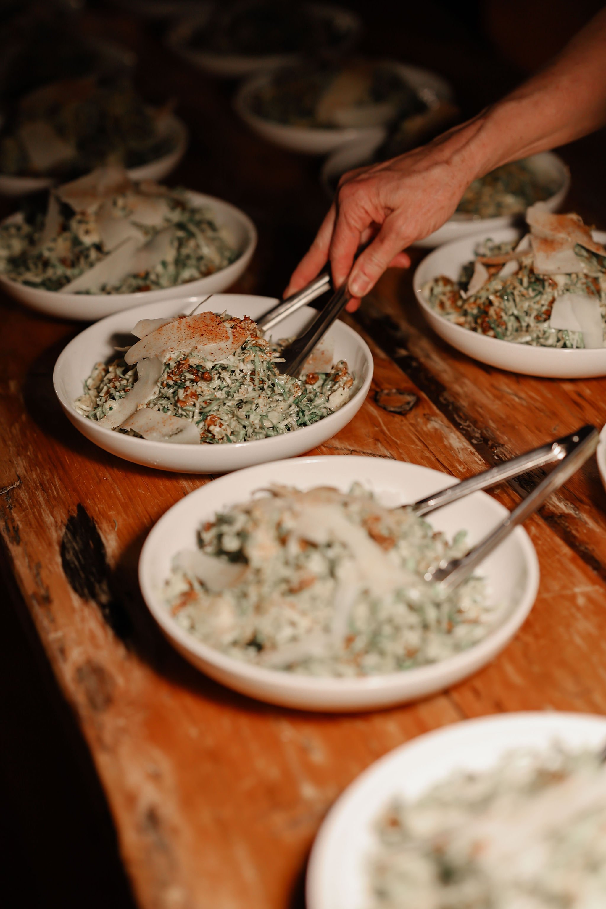 Multiple white bowls filled with a leafy salad topped with slices of cheese, placed on a rustic wooden table.
