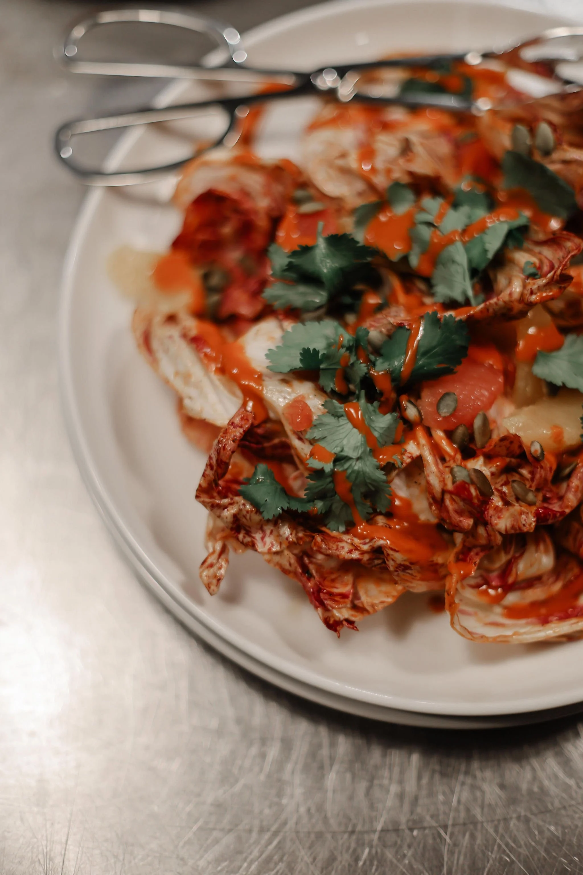 A plate of shredded chicken topped with cilantro, pumpkin seeds, sliced tomatoes, and drizzled with hot sauce.