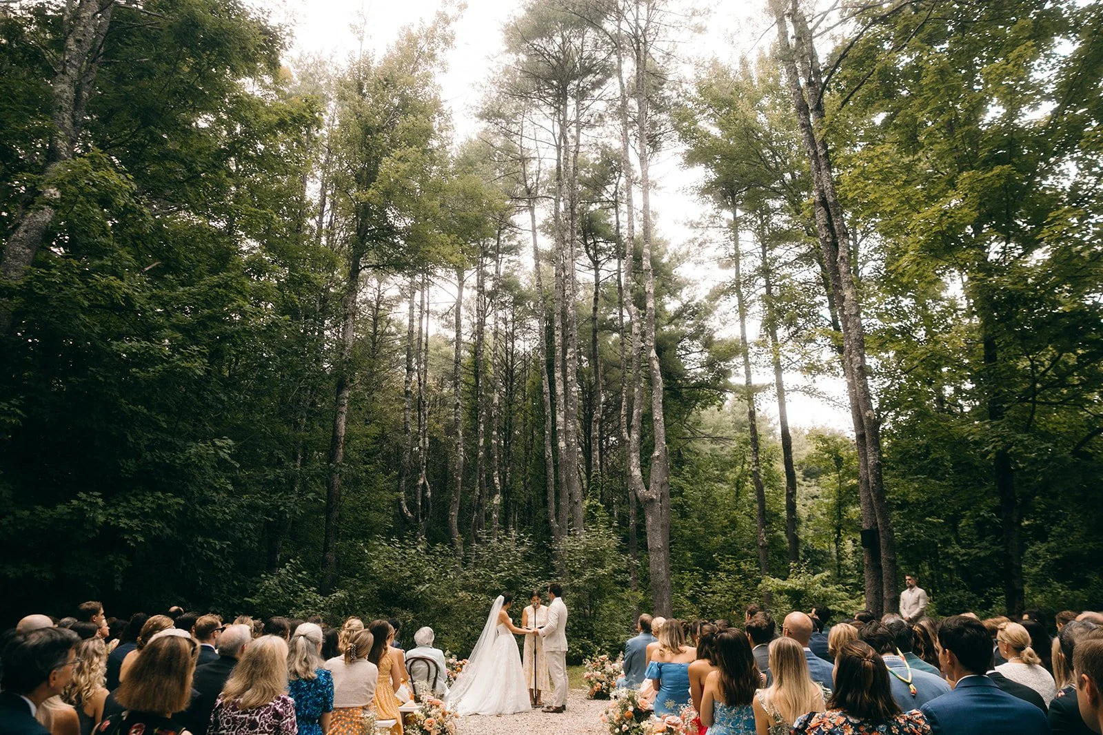 Outdoor wedding ceremony in a forest with guests seated and a bride and groom at the altar.