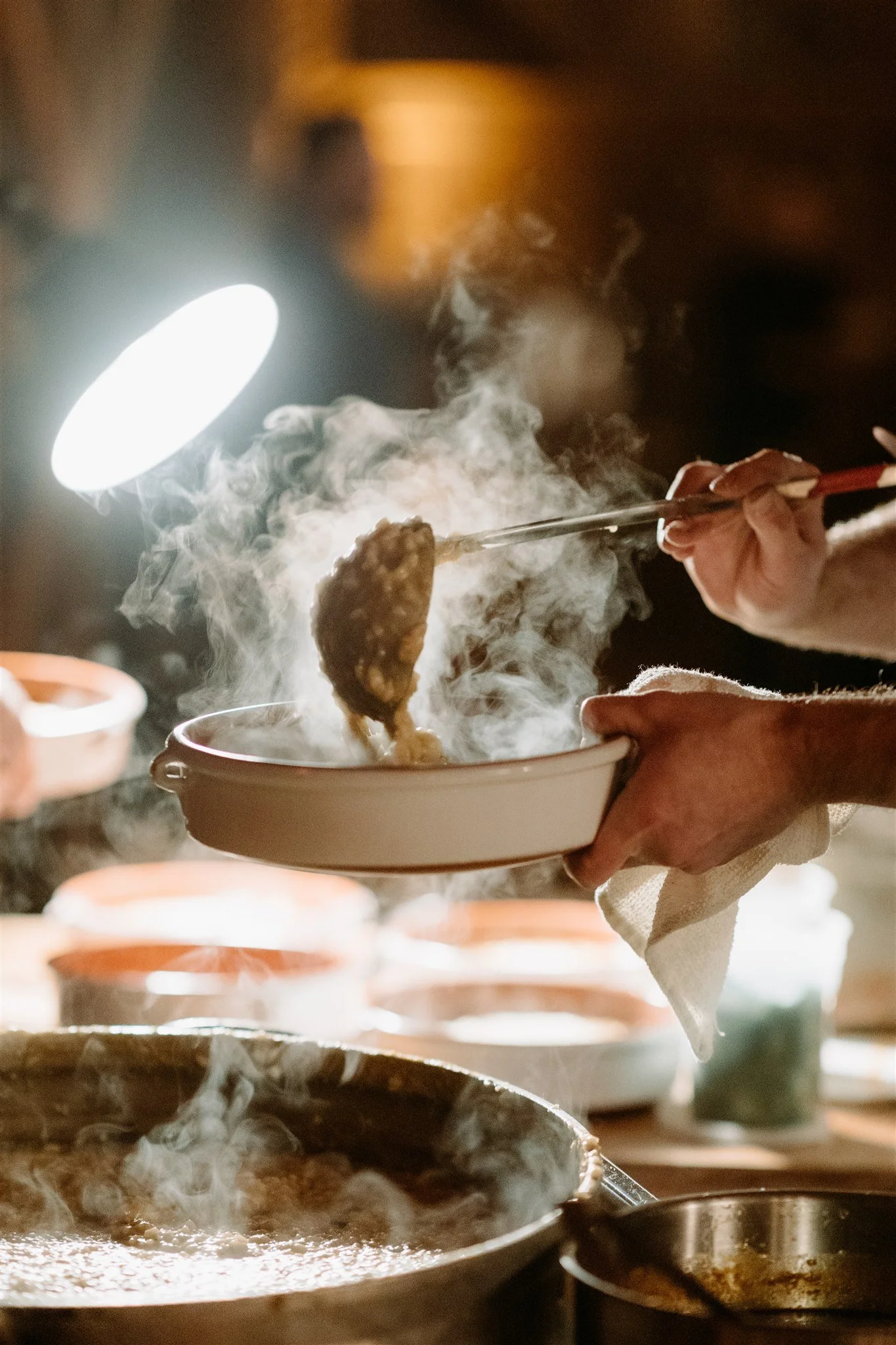 Person holding a bowl with steaming food, using chopsticks to serve.
