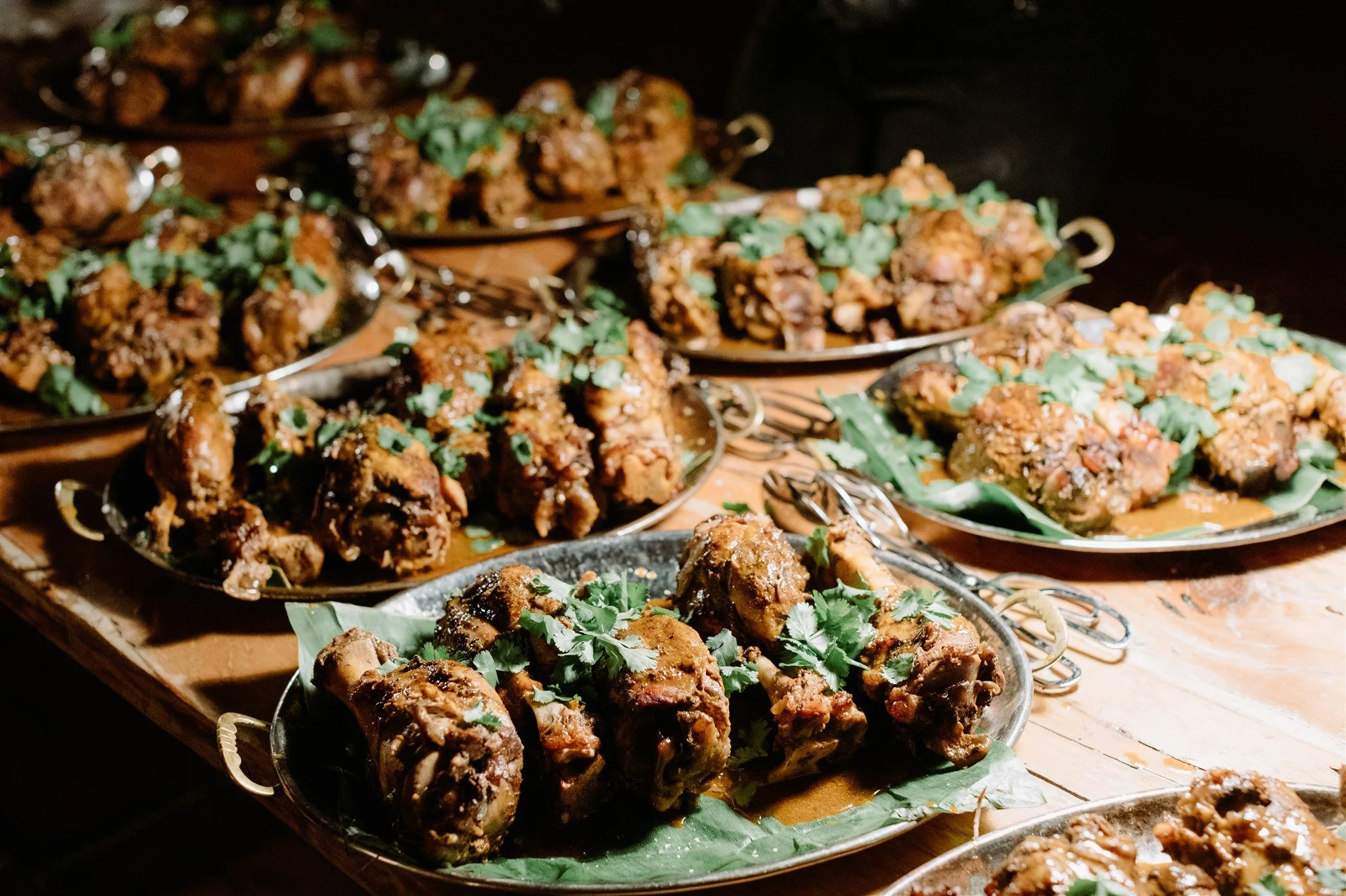 Plates of cooked chicken drumsticks garnished with cilantro, with a dark background and a wooden table.
