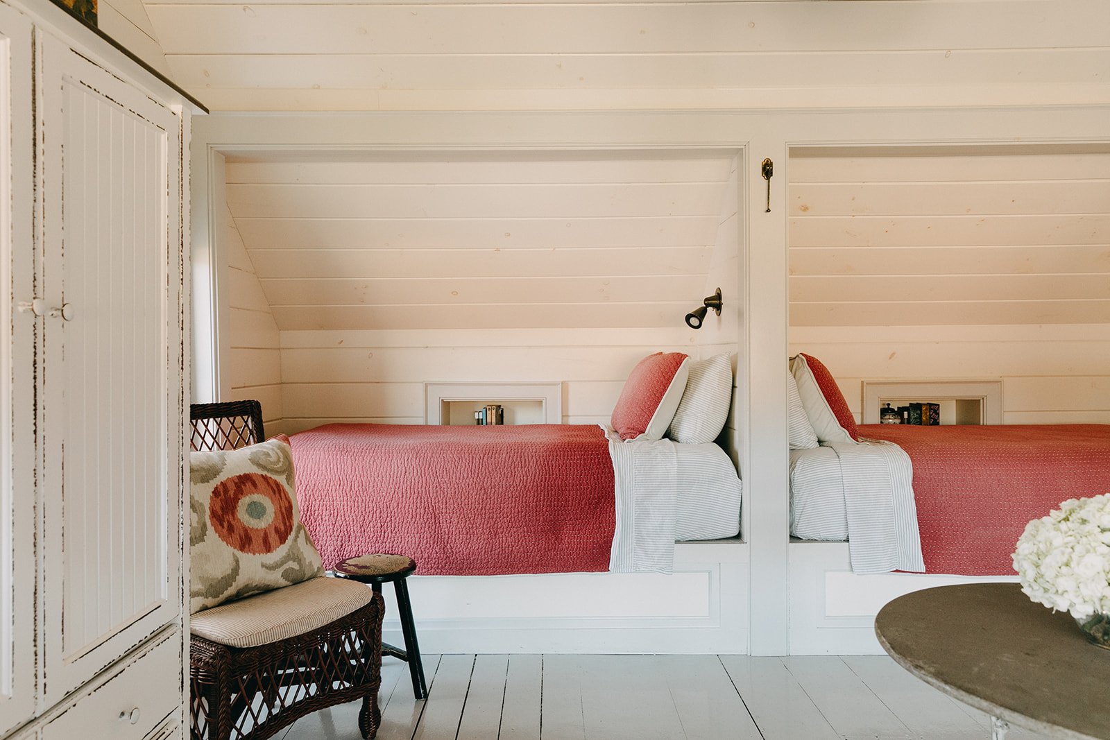 Bedroom with two beds separated by a white wall, each with pink bedding and white pillows, against white paneled walls and sloped ceiling.