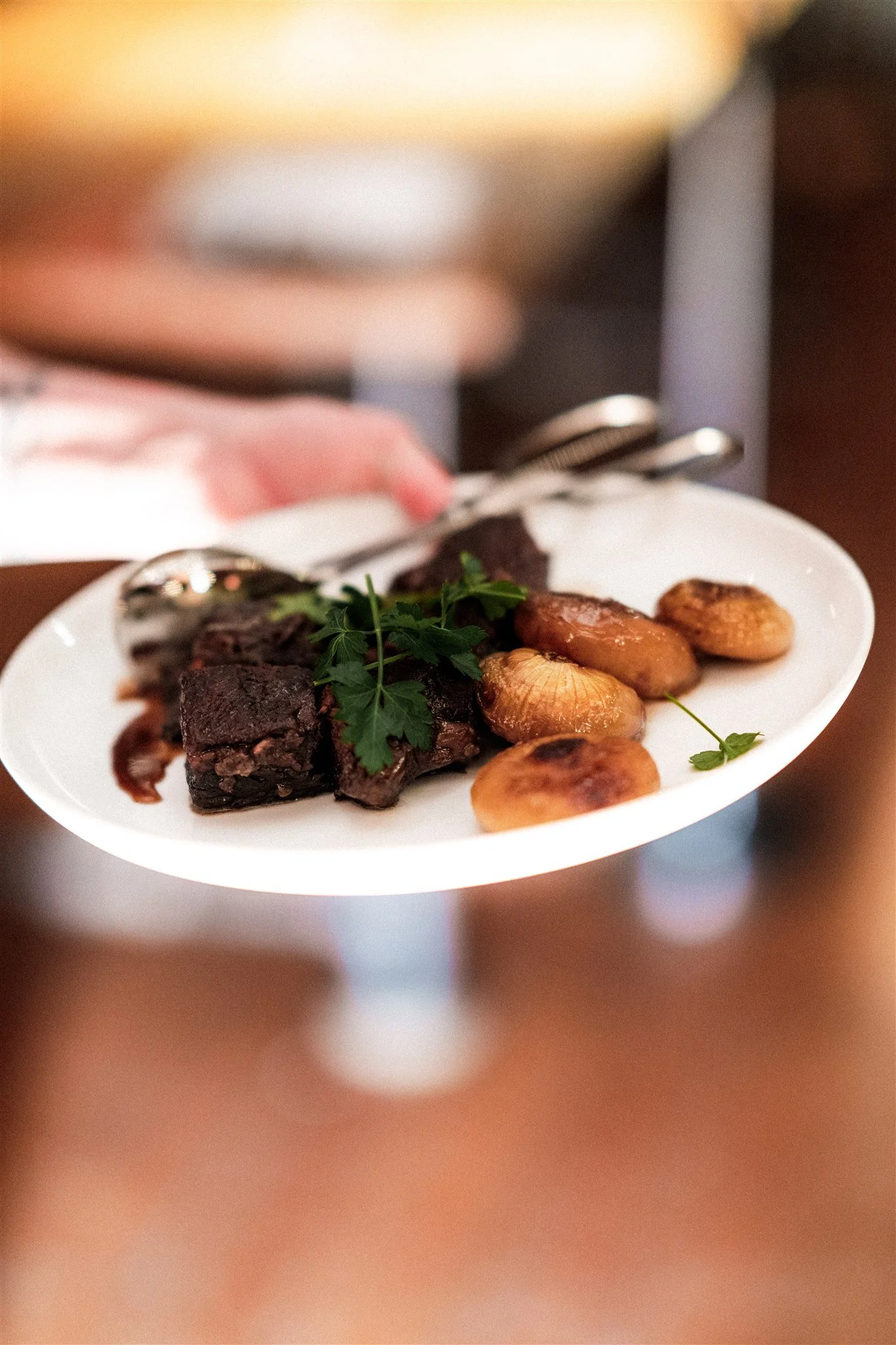 A white plate with meat, fried potatoes, and garnished with fresh herbs.