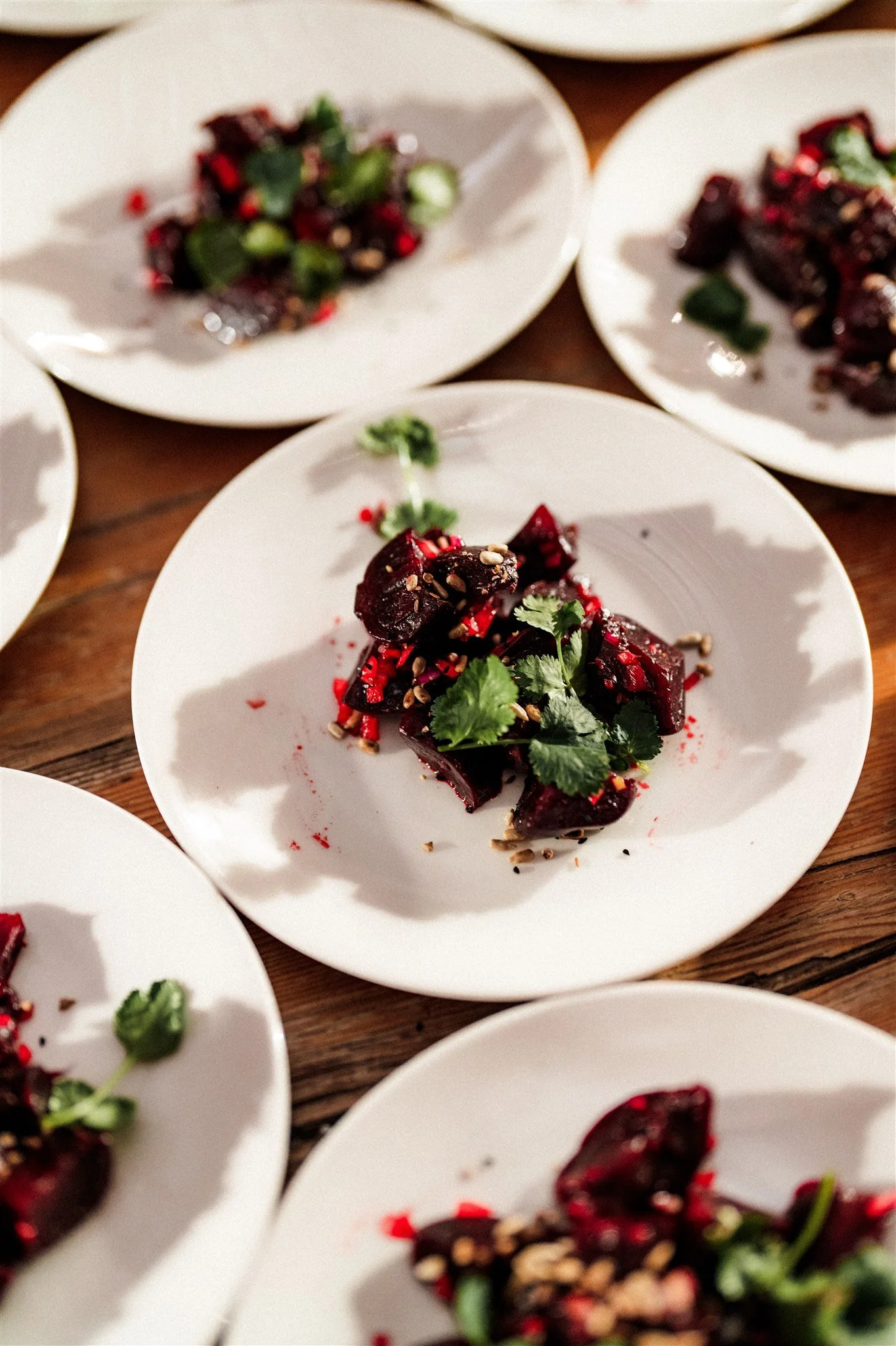 Plates of sliced dark purple beetroot garnished with cilantro, red pepper flakes, and sunflower seeds on a wooden table.
