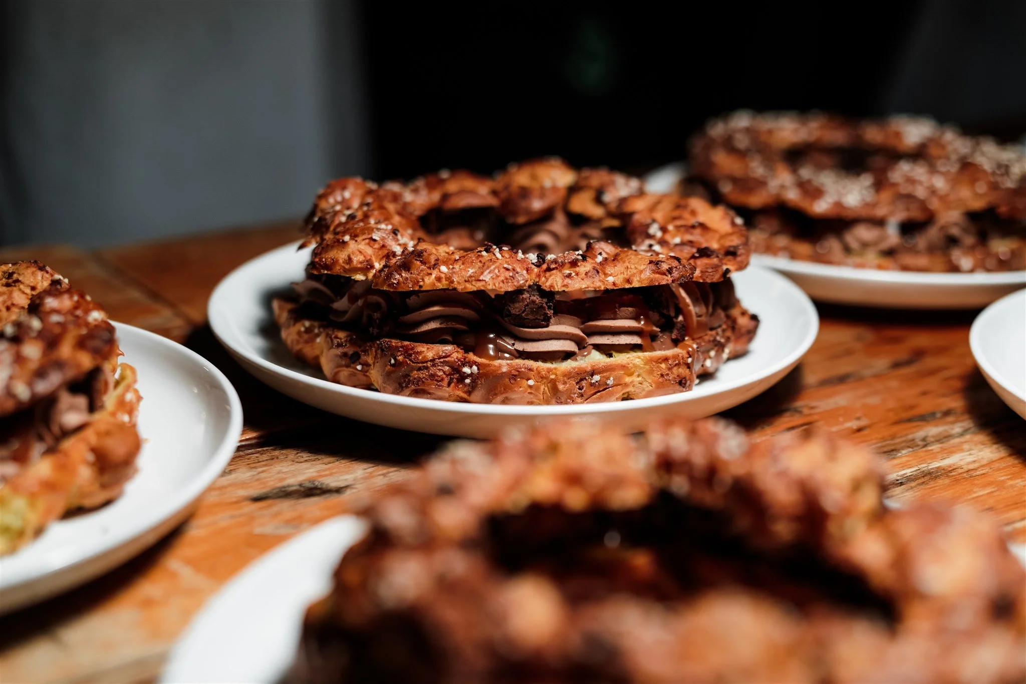 Chocolate croissant sandwiches with chocolate filling on white plates, on a wooden table.