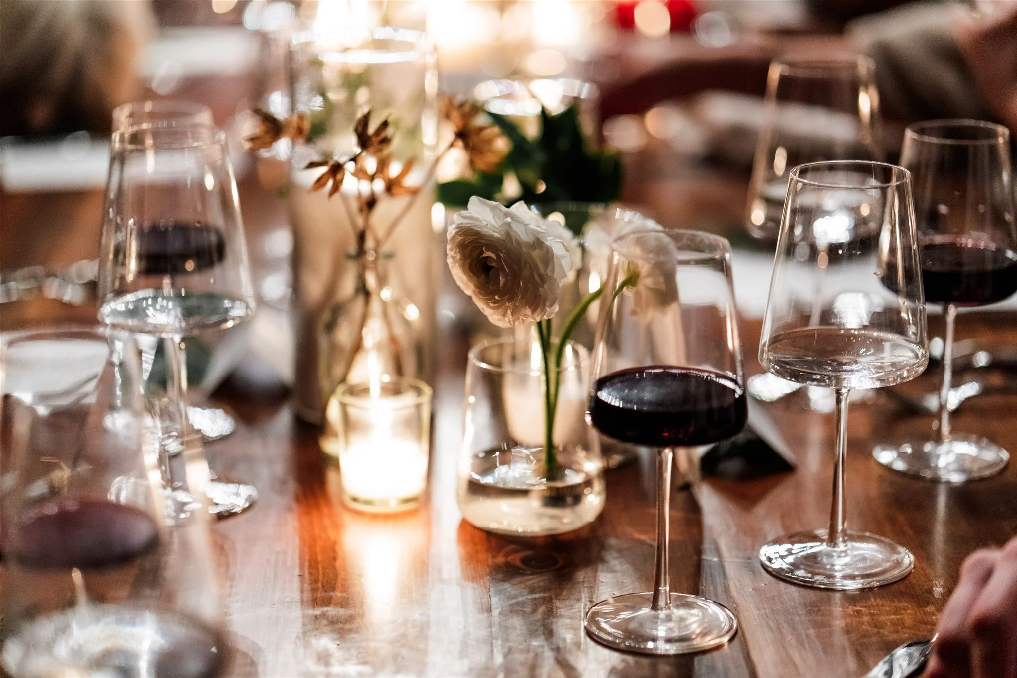 A dining table with wine glasses, floral centerpieces, and a lit candle in a glass holder, creating an elegant setting.